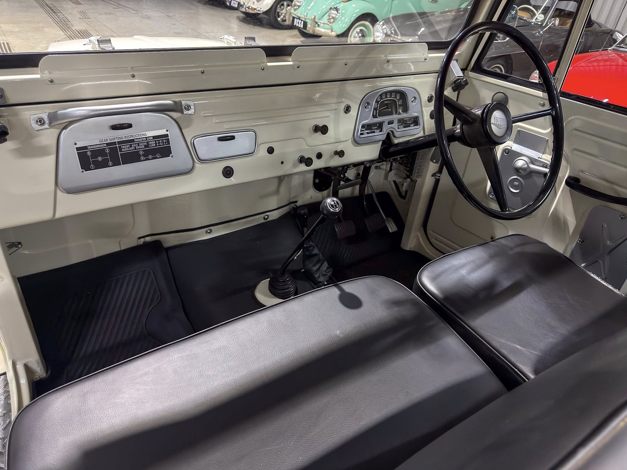 Interior of a vintage car showing a gray dashboard, large circular steering wheel, and manual gear lever in the foreground.