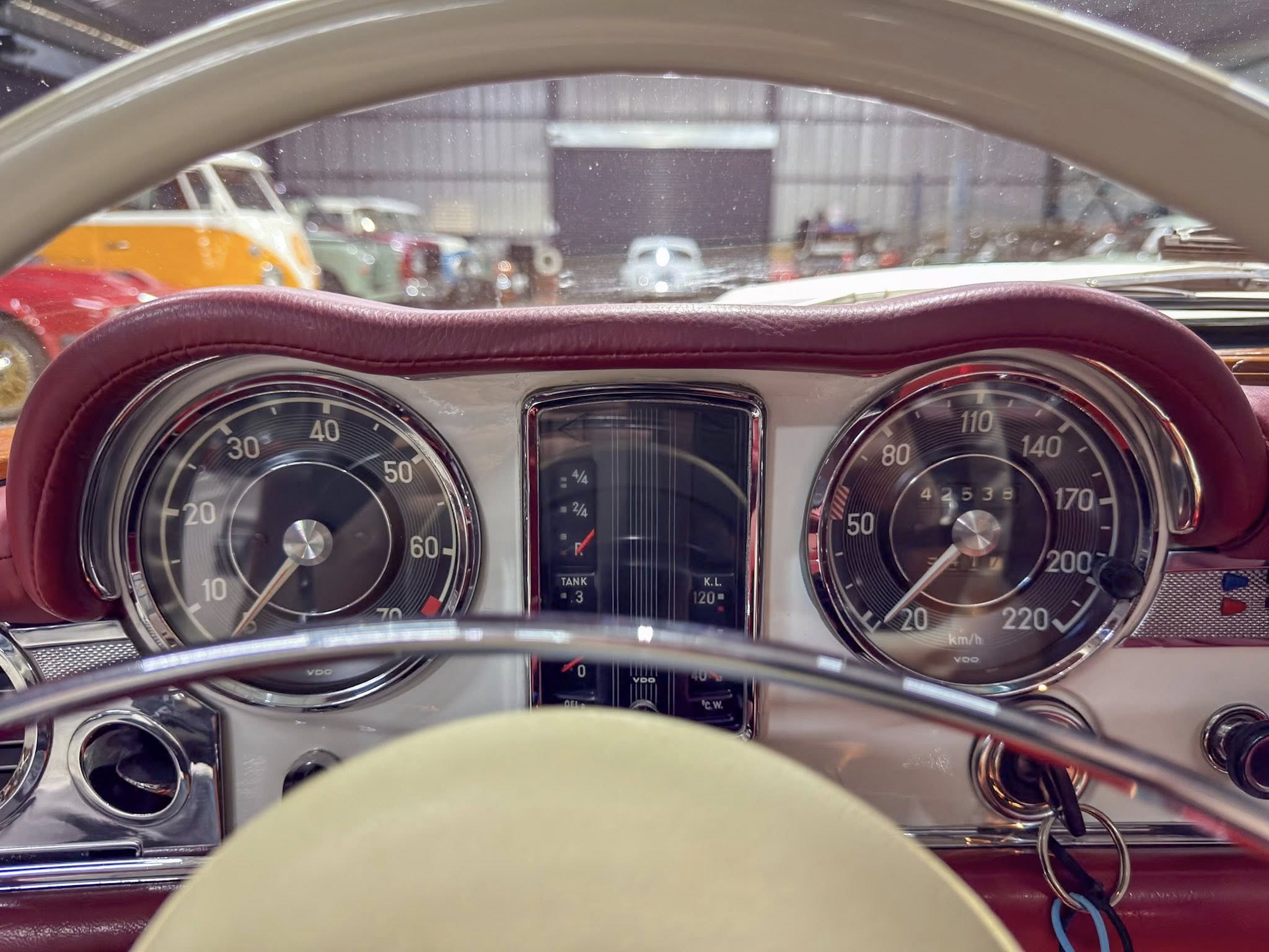 Close-up of a vintage car dashboard with large analog speedometer gauges and burgundy upholstery from the driver's seat.