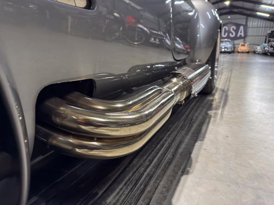 Close-up of chrome side exhaust pipes on a vintage gray car in a showroom.
