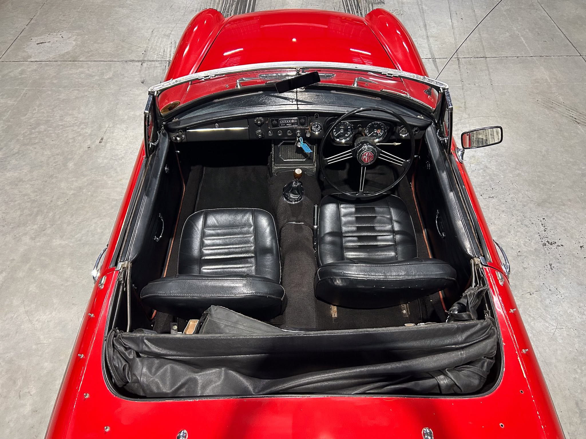 Top-down view of a red vintage convertible showing black leather seats and classic dashboard with round gauges and steering wheel.