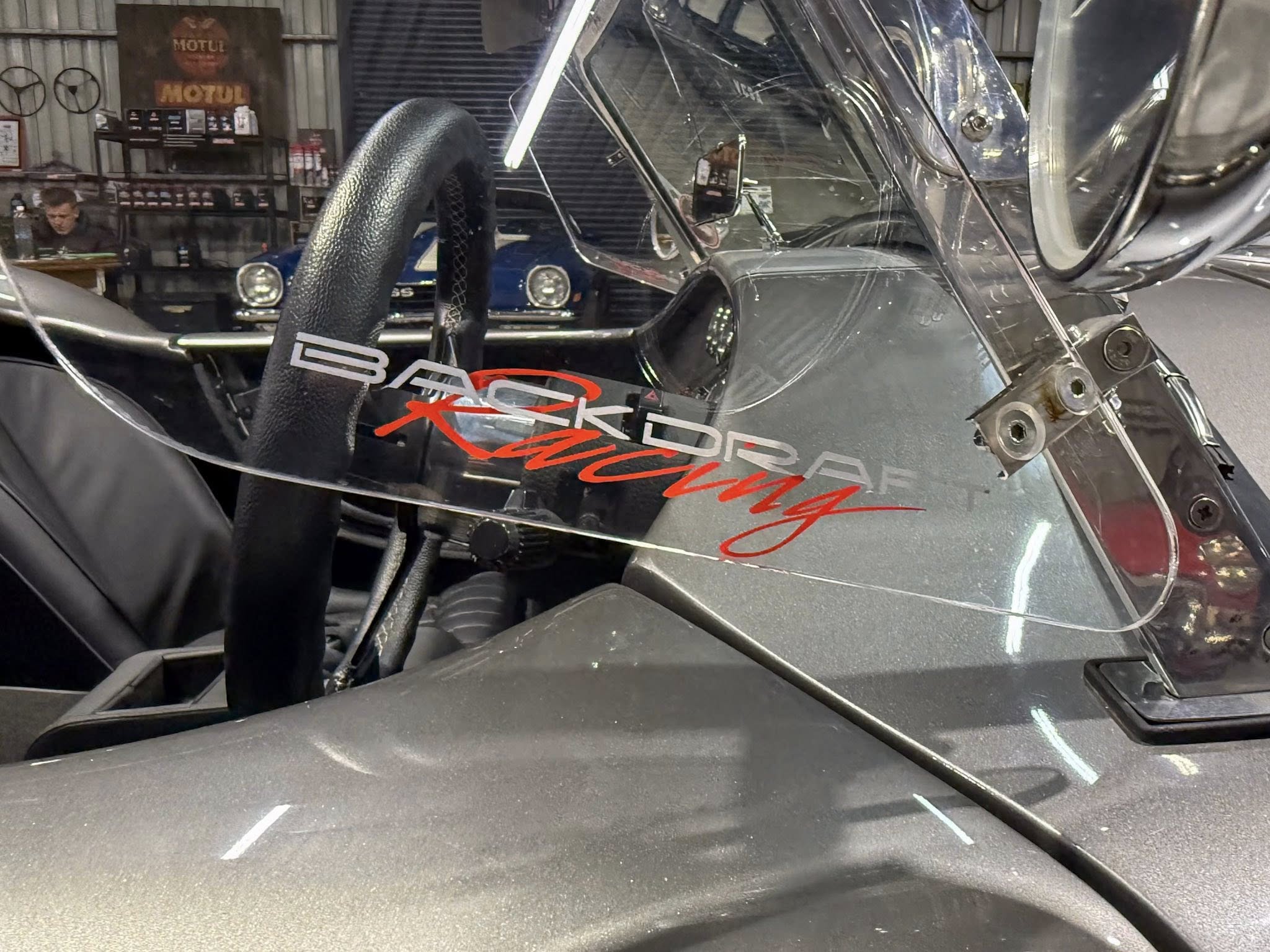 Close-up of a damaged race car cockpit with a cracked windshield and exposed interior in a workshop.