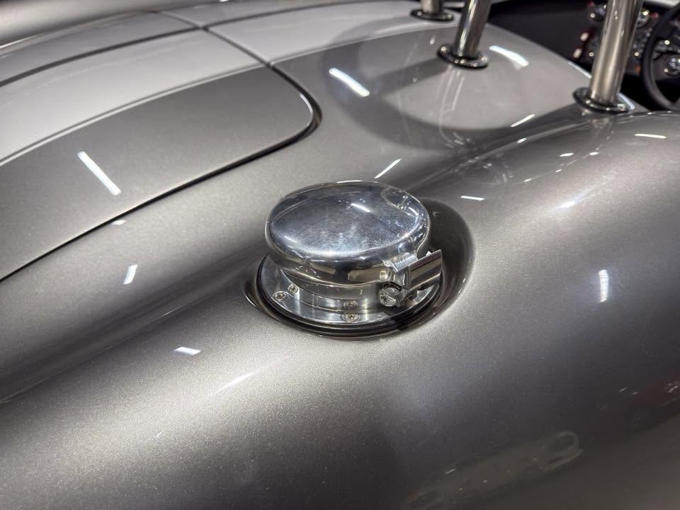 Chrome fuel cap on a metallic silver vintage car body, with reflections on the polished surface.