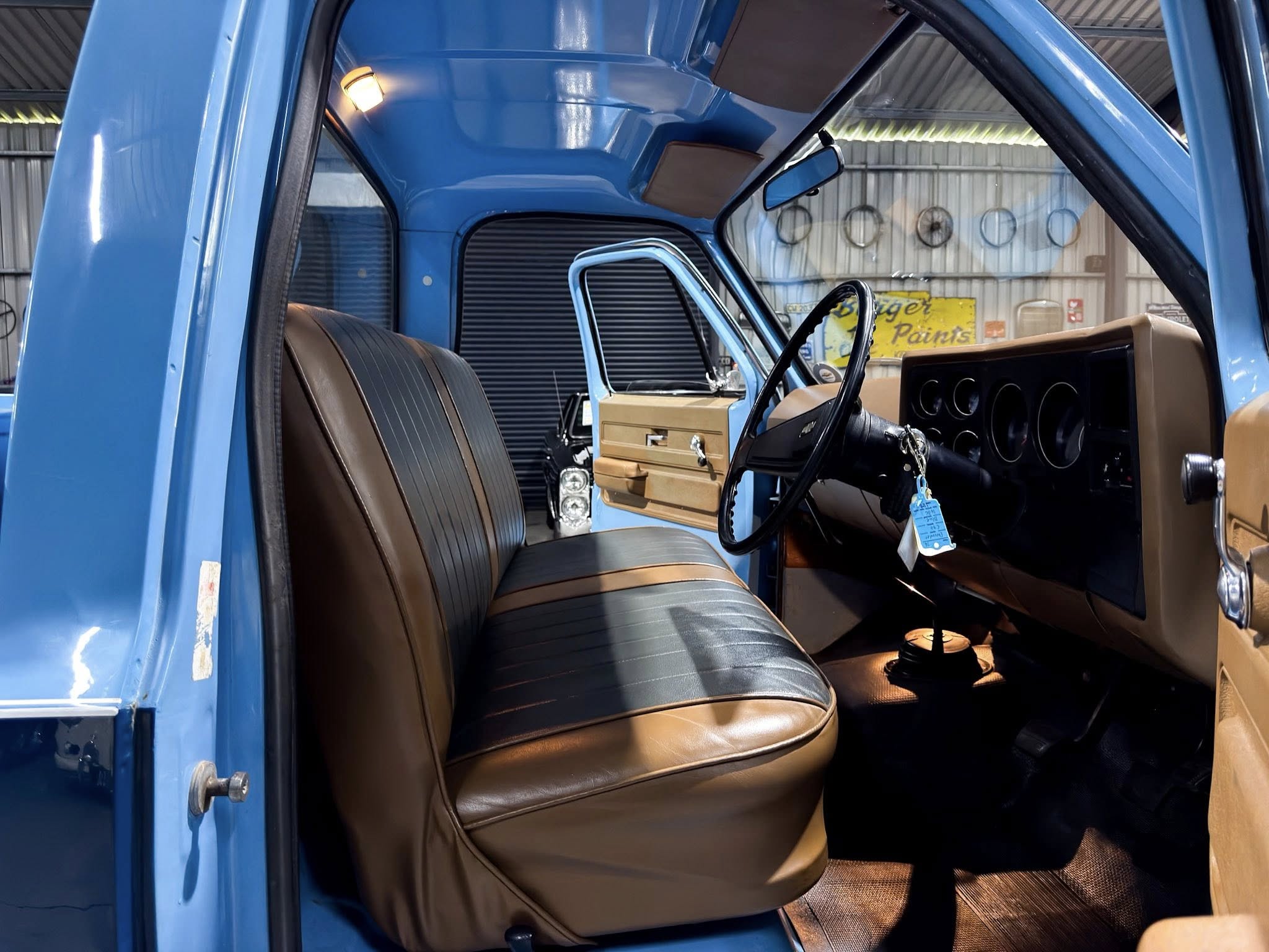 Interior of a blue pickup truck with brown vinyl seats, open driver’s door, and a black steering wheel visible from the passenger side window area