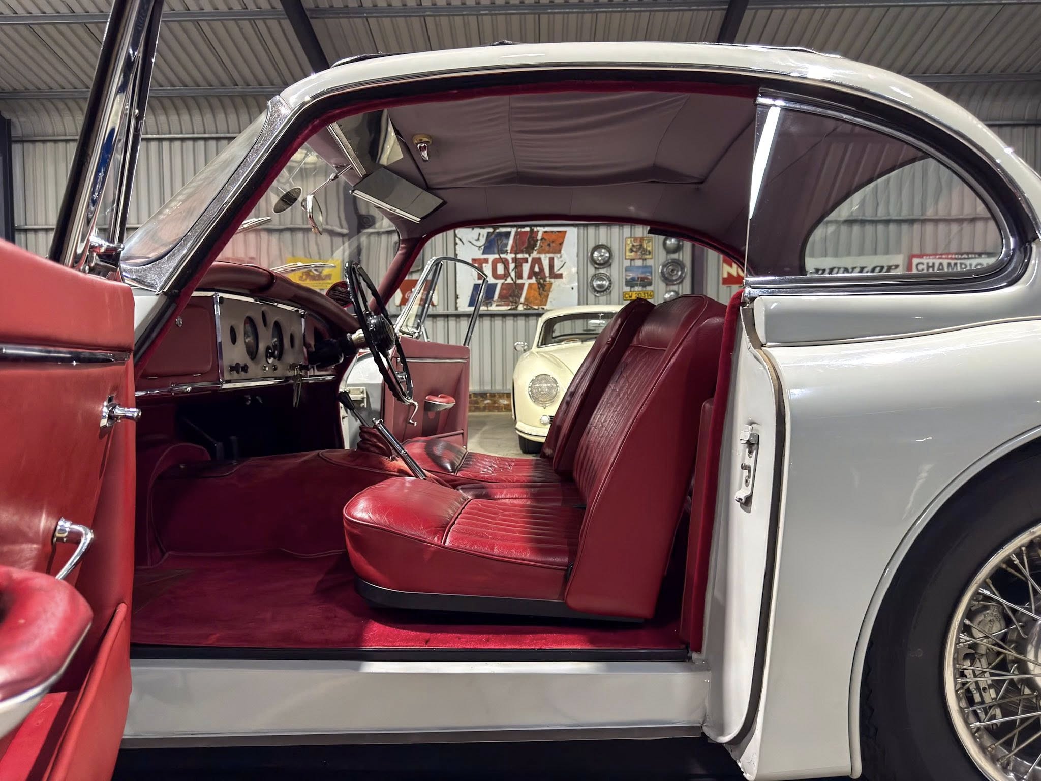 Interior of a vintage car with red leather seats and open door, showing chrome trim and dashboard in a showroom setting.