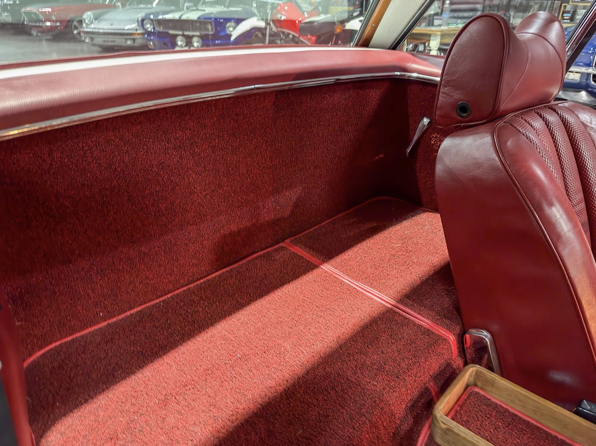 Red leather car interior with plush seats and red carpet, visible showroom cars through the window.