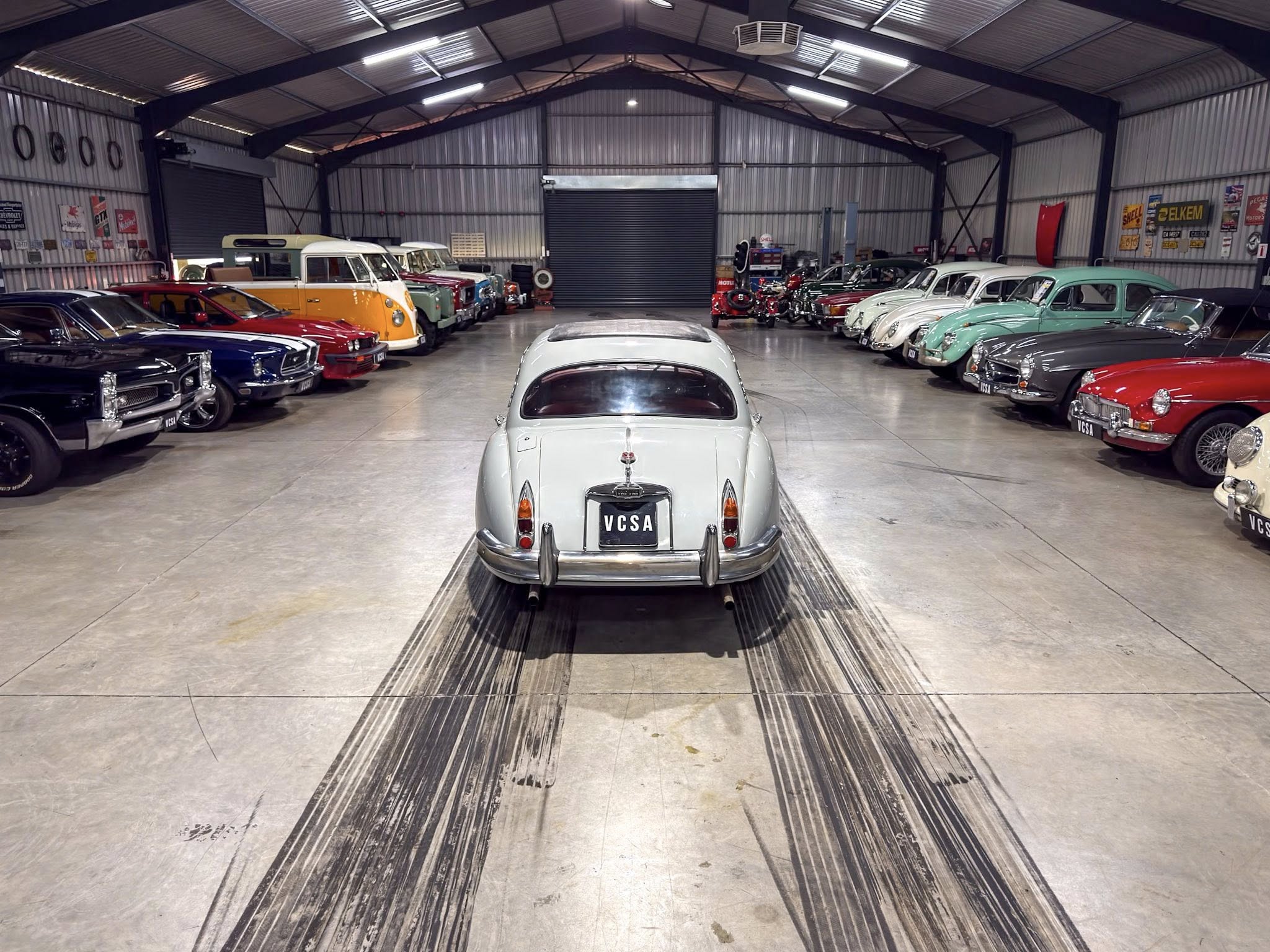 Vintage car showroom with rows of classic cars along both sides and a silver rear-end vehicle in the center foreground