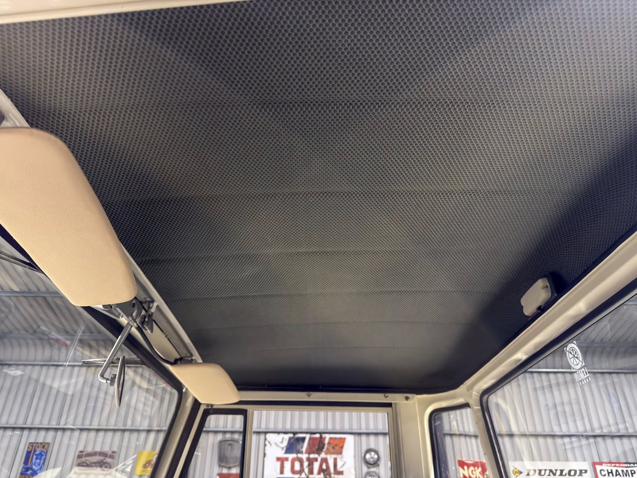 Interior view of a vehicle cabin ceiling with a gray perforated headliner and beige grab handles hanging from the top
