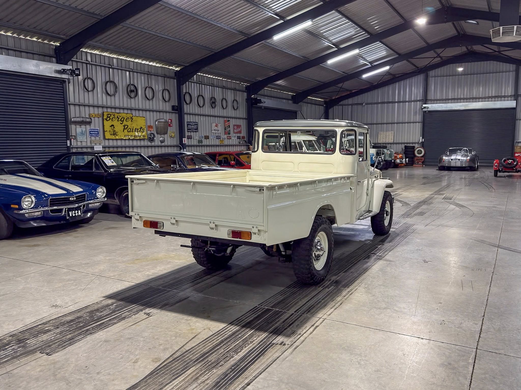 Interior of a vintage car showroom with classic cars lined along the walls and a white pickup in the foreground