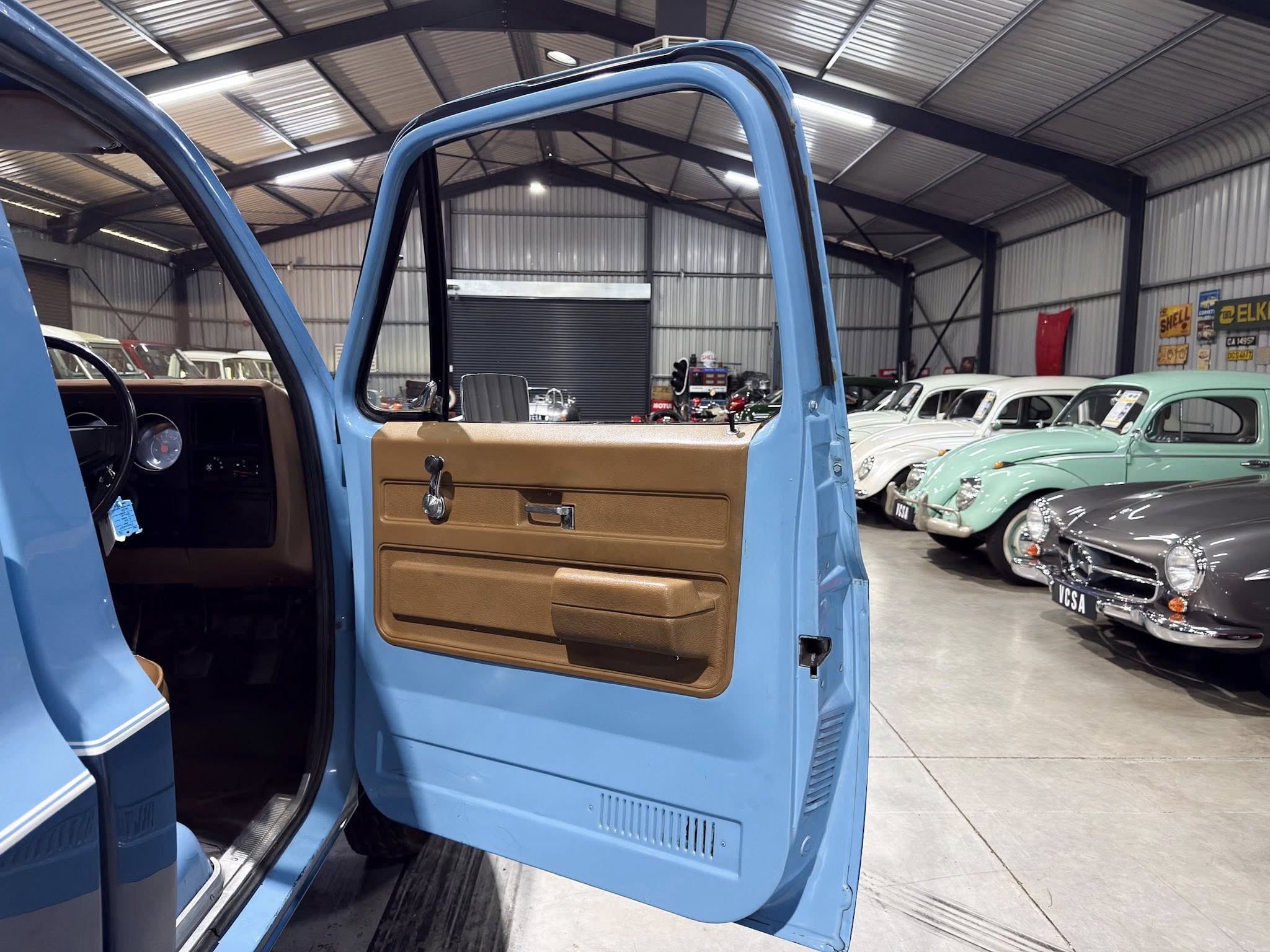 Open blue car door showing brown interior in a vehicle showroom with a row of vintage cars in pastel colors in the background