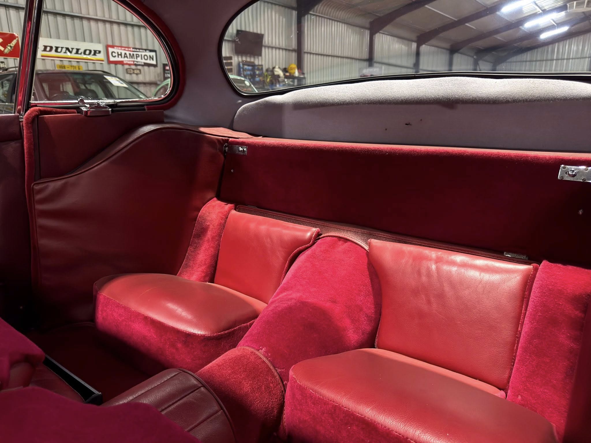 Red leather rear seats and door panels of a vintage car, viewed from the back seat.