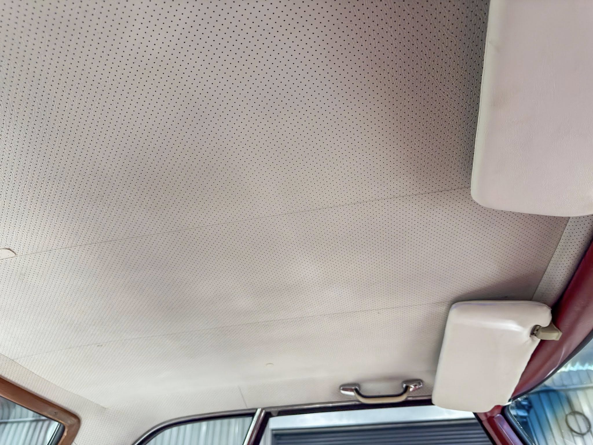 Beige perforated car headliner with a sun visor and grab handle along the ceiling, seen from the passenger side.