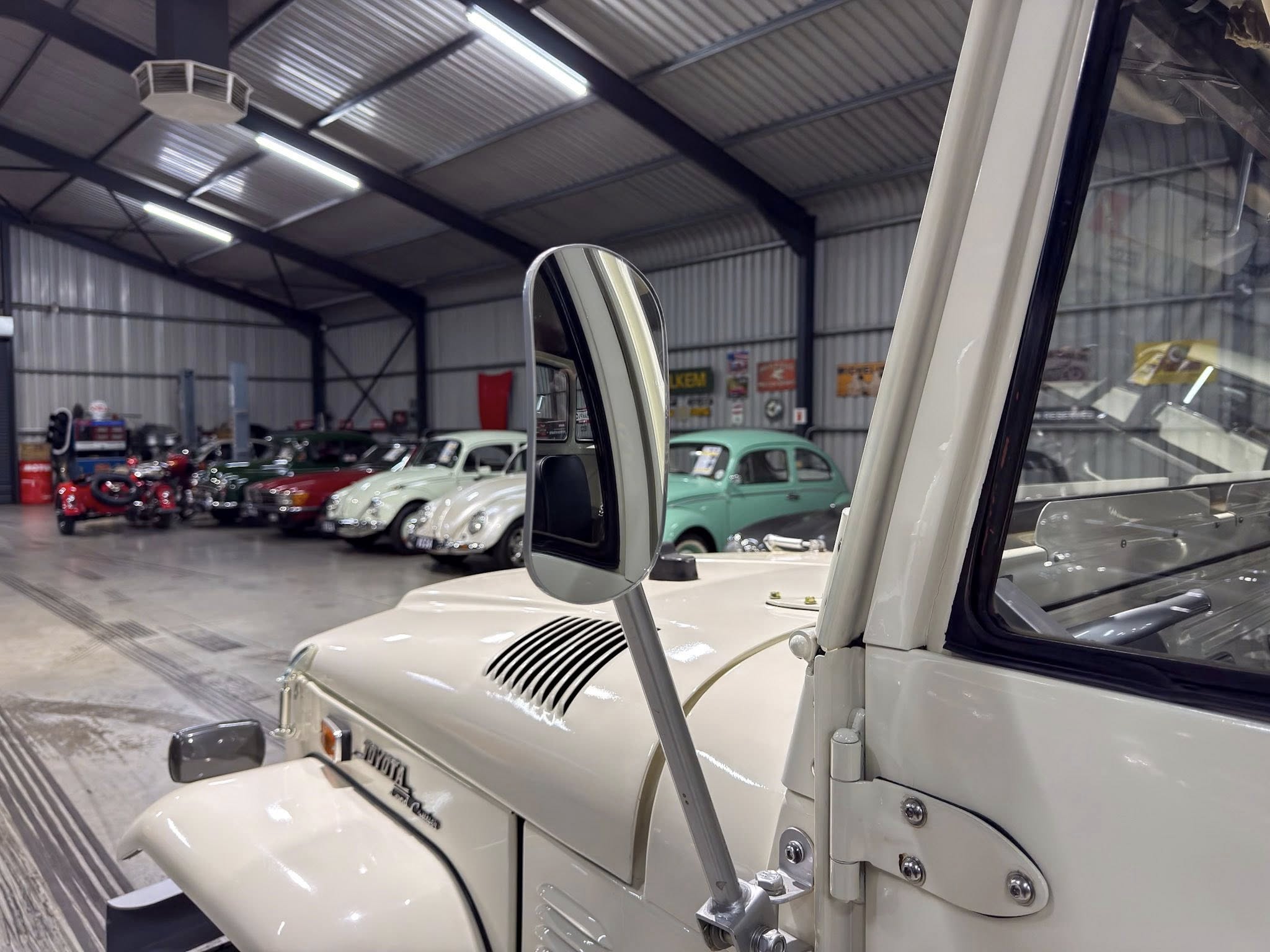 View from the driver's side of a cream-colored vintage car inside a showroom, with rows of classic cars in the background.