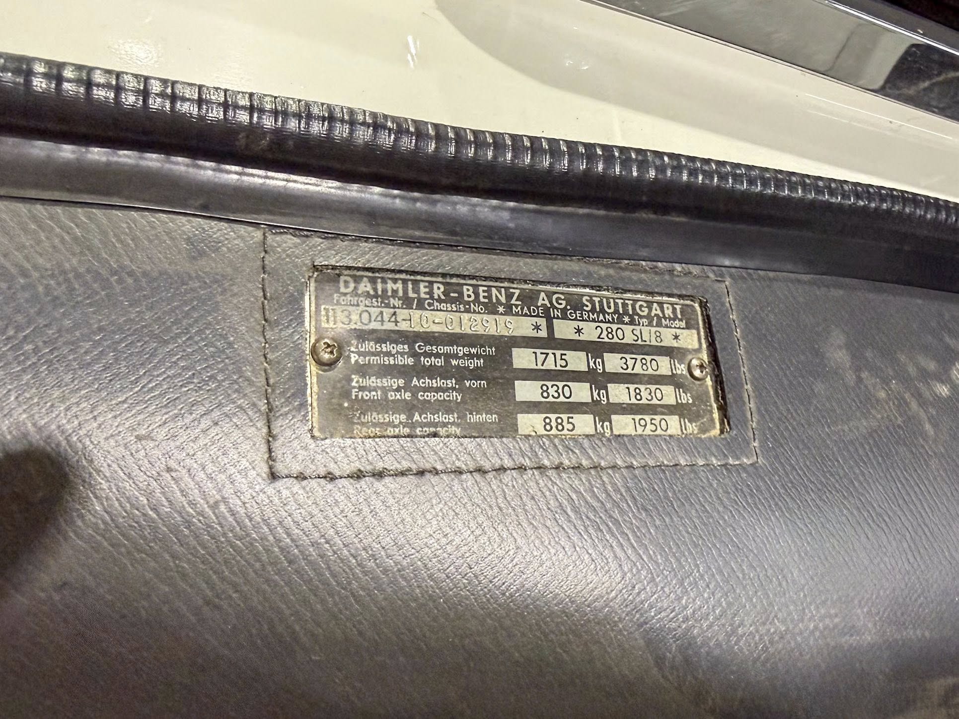 Vehicle data plate mounted in a car interior showing manufacturer Daimler-Benz Stuttgart and weight/axle specifications (kg).