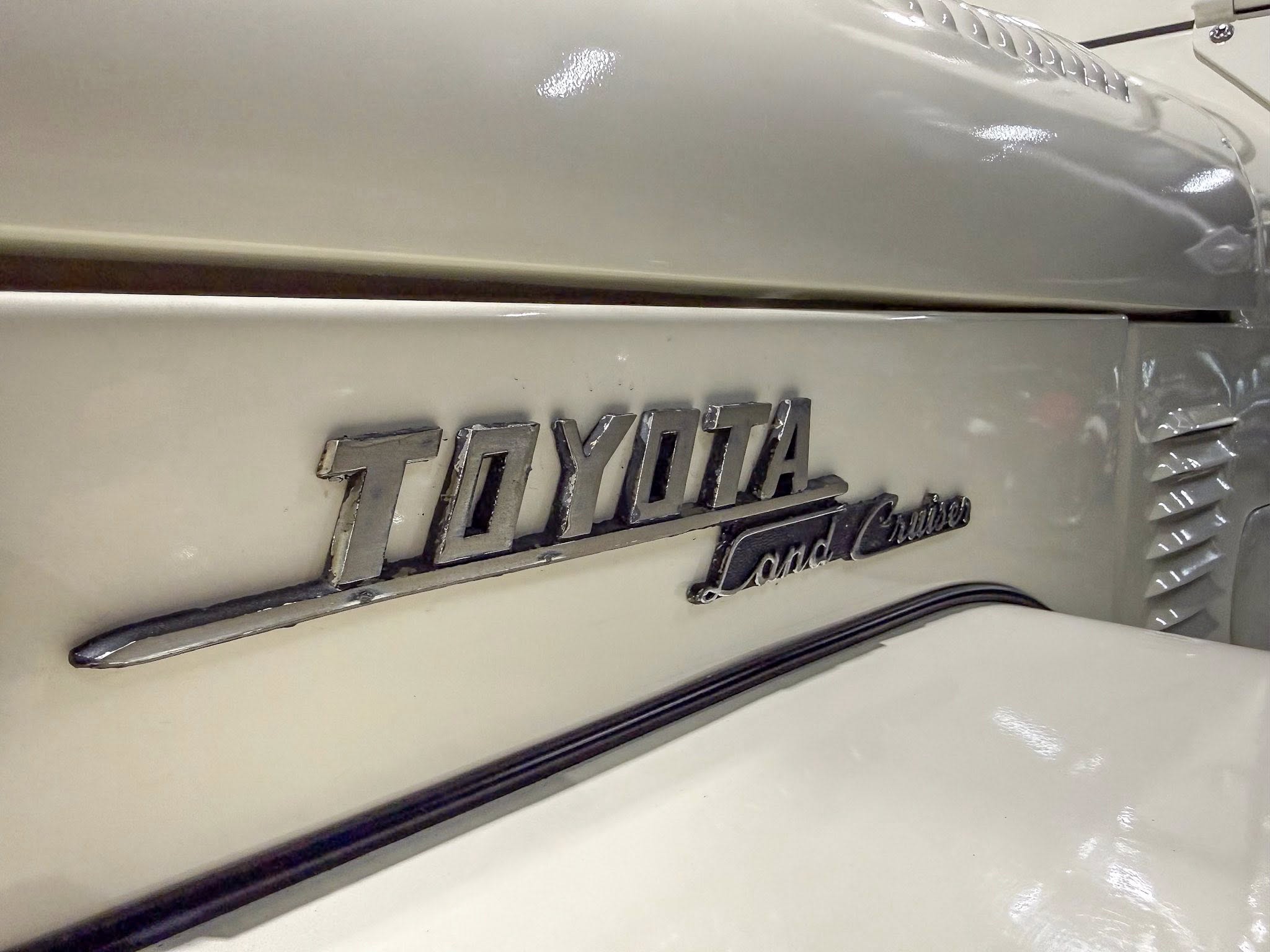 Chrome Toyota emblem with 'Land Cruiser' script on a light-colored vintage SUV rear badge area.