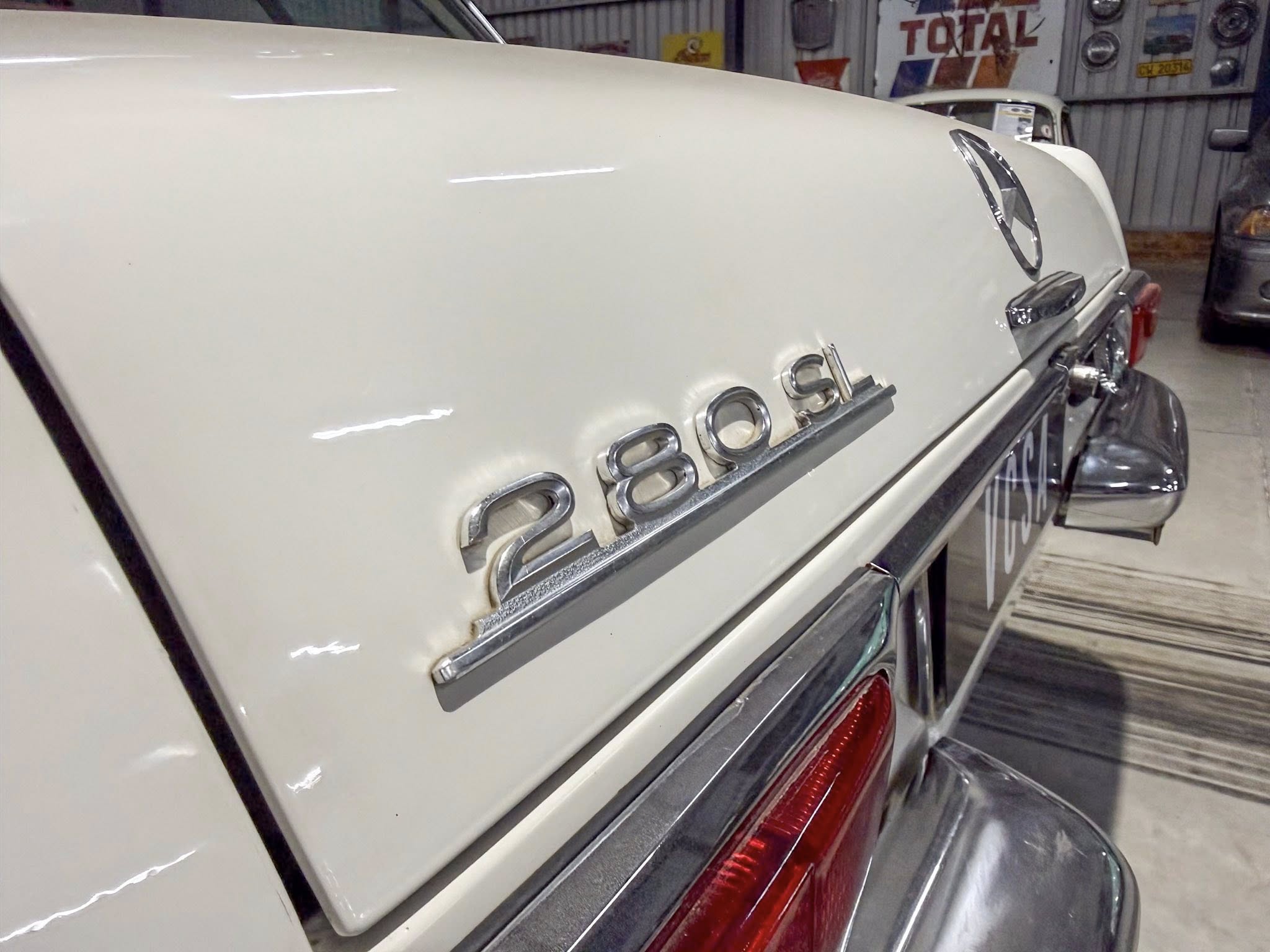 Rear end of a white vintage Mercedes car with chrome trim and red tail lights in an indoor setting.