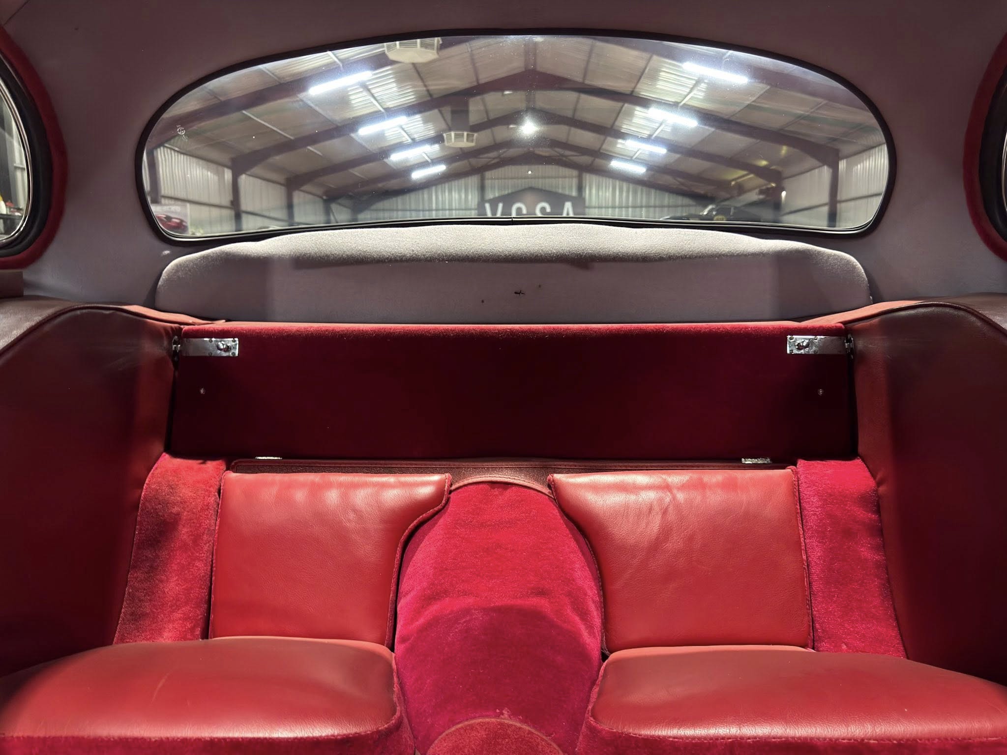 Red leather car backseat with a curved rear window; a warehouse is visible through the glass.