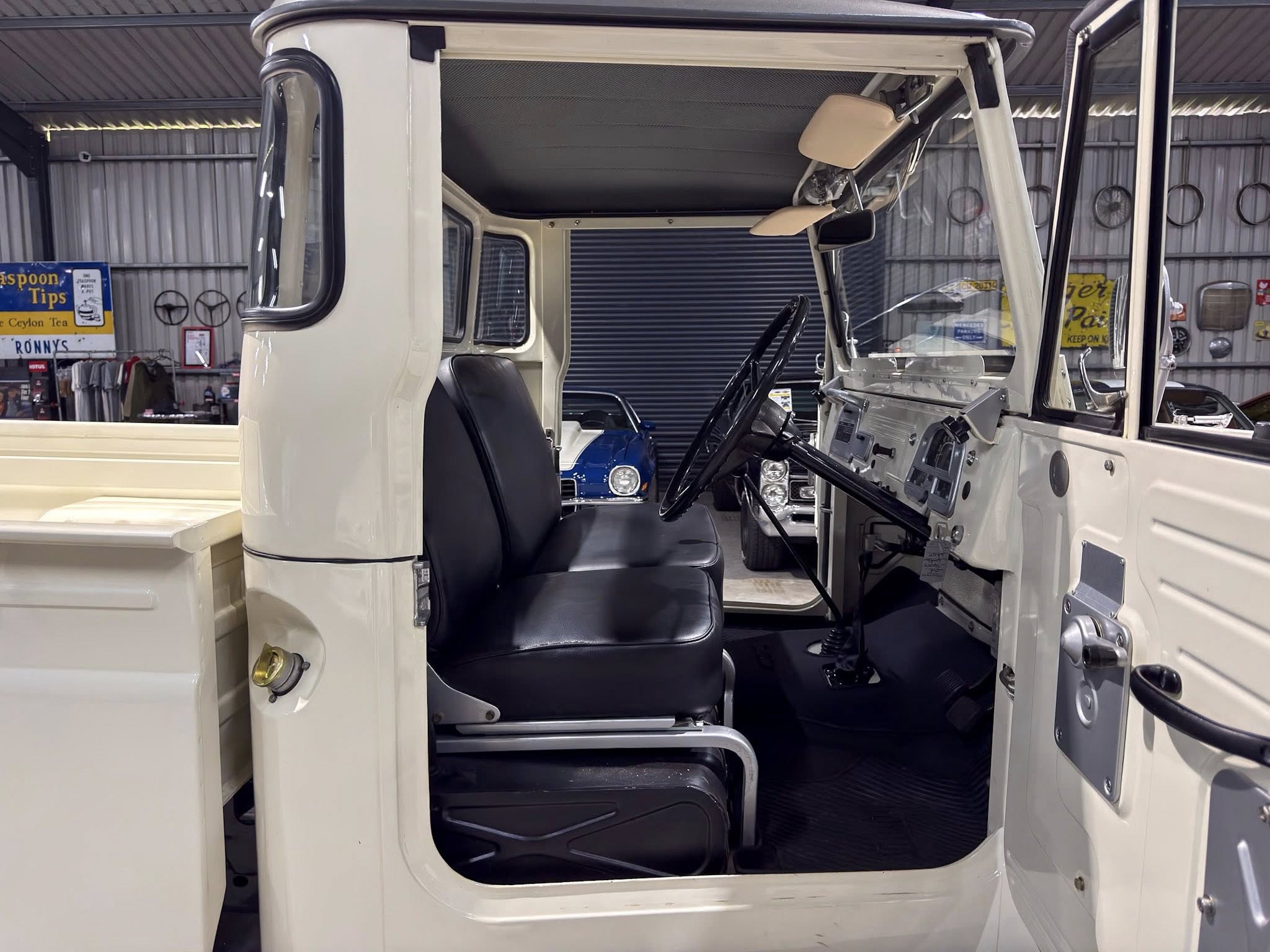 Inside view of a white truck cab with black seats, large steering wheel, and beige sun visors in a showroom setting