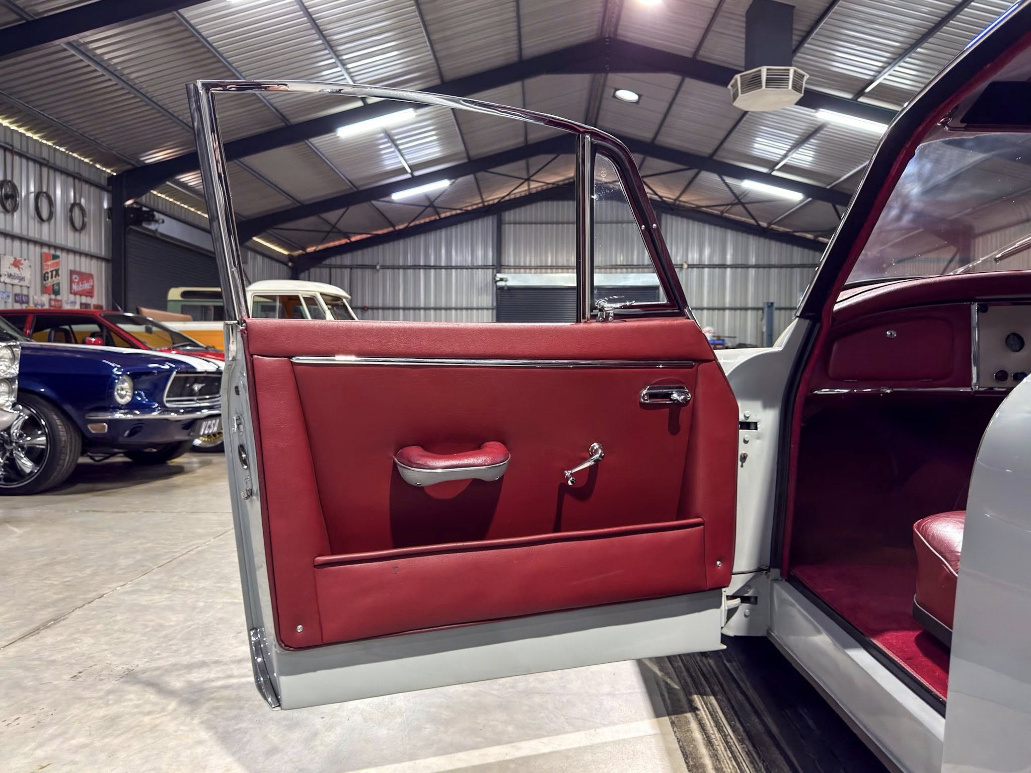 Open car door of a red vintage car inside a showroom or garage with other classic cars in the background.