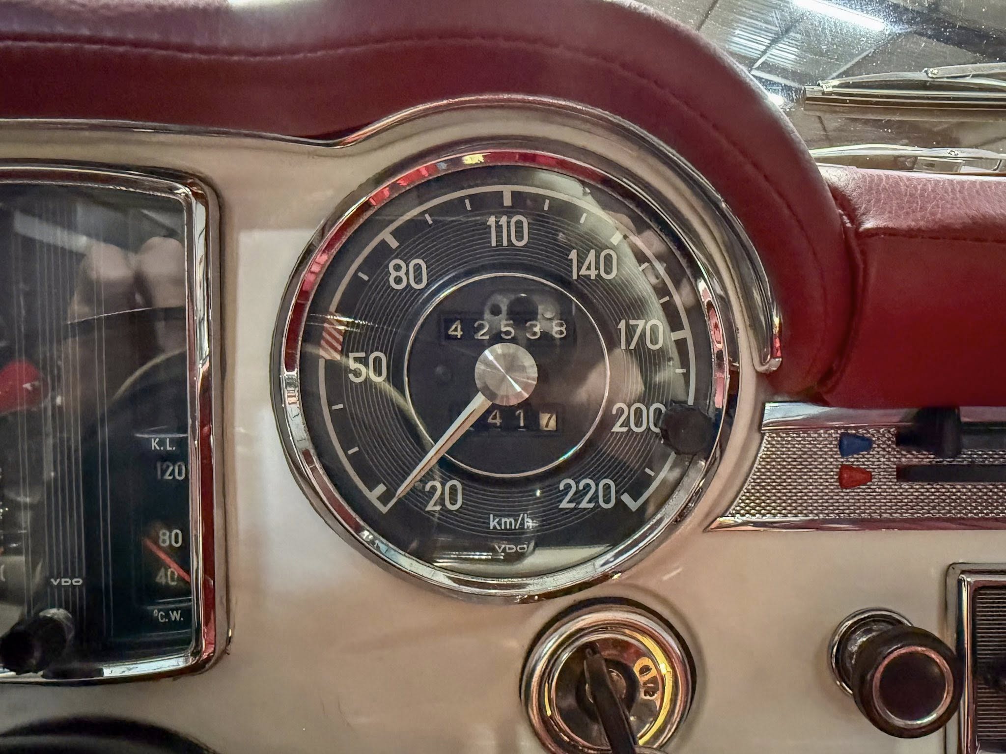 Close-up of vintage car dashboard speedometer, numbered up to 220 km/h, with red leather surround.