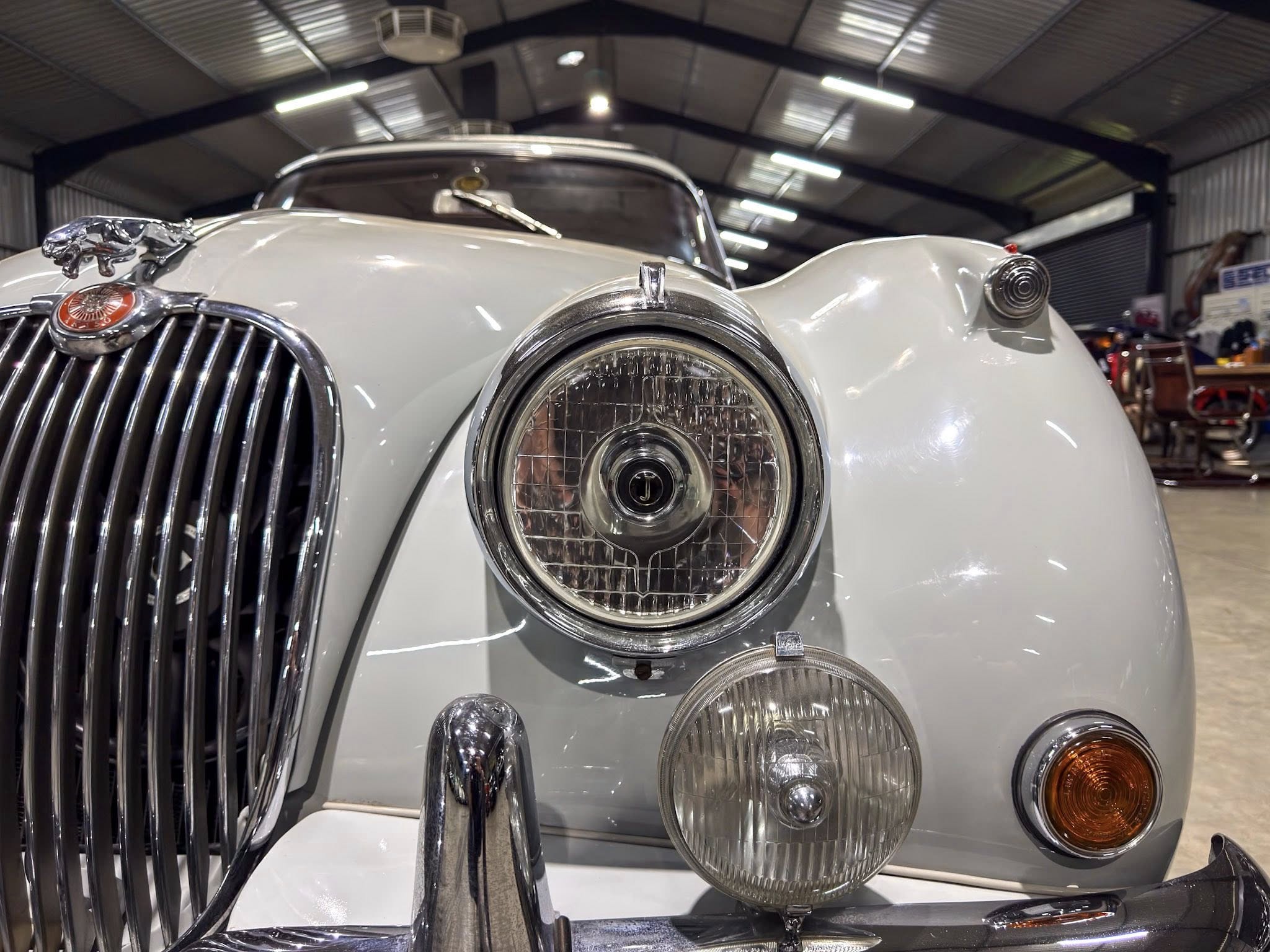Close-up of a vintage car's front end with chrome grille, round headlight, and hood ornament in a showroom.
