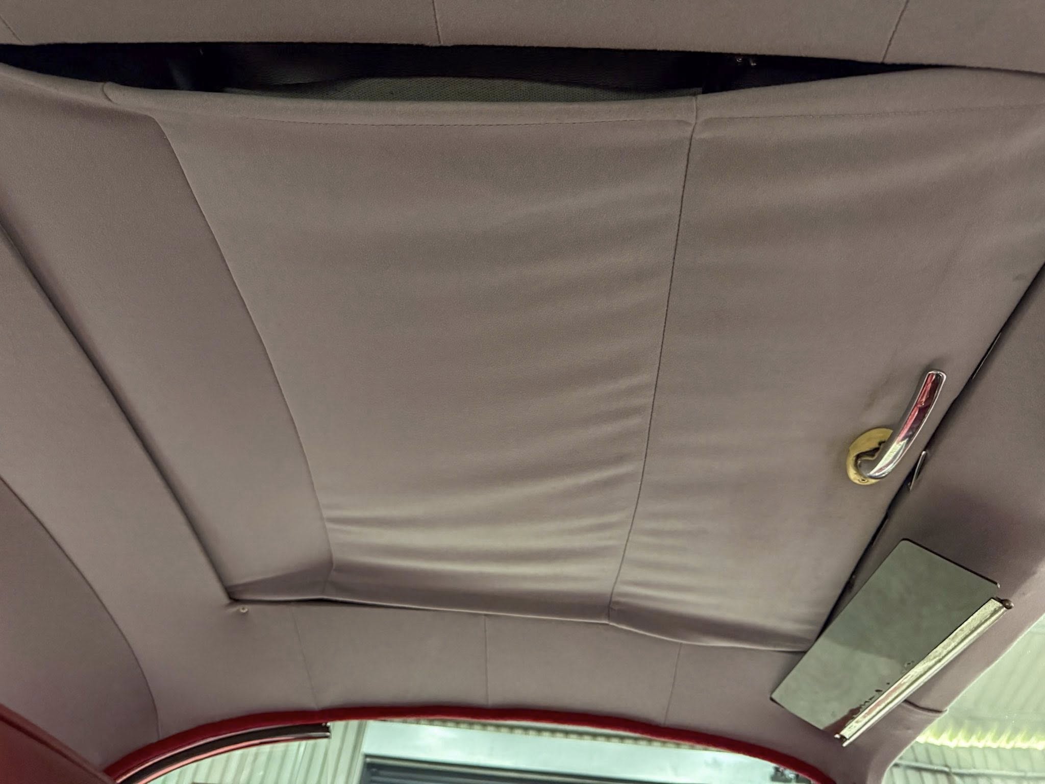 Beige car headliner with stitched panels; a red seat belt buckle appears at bottom right.
