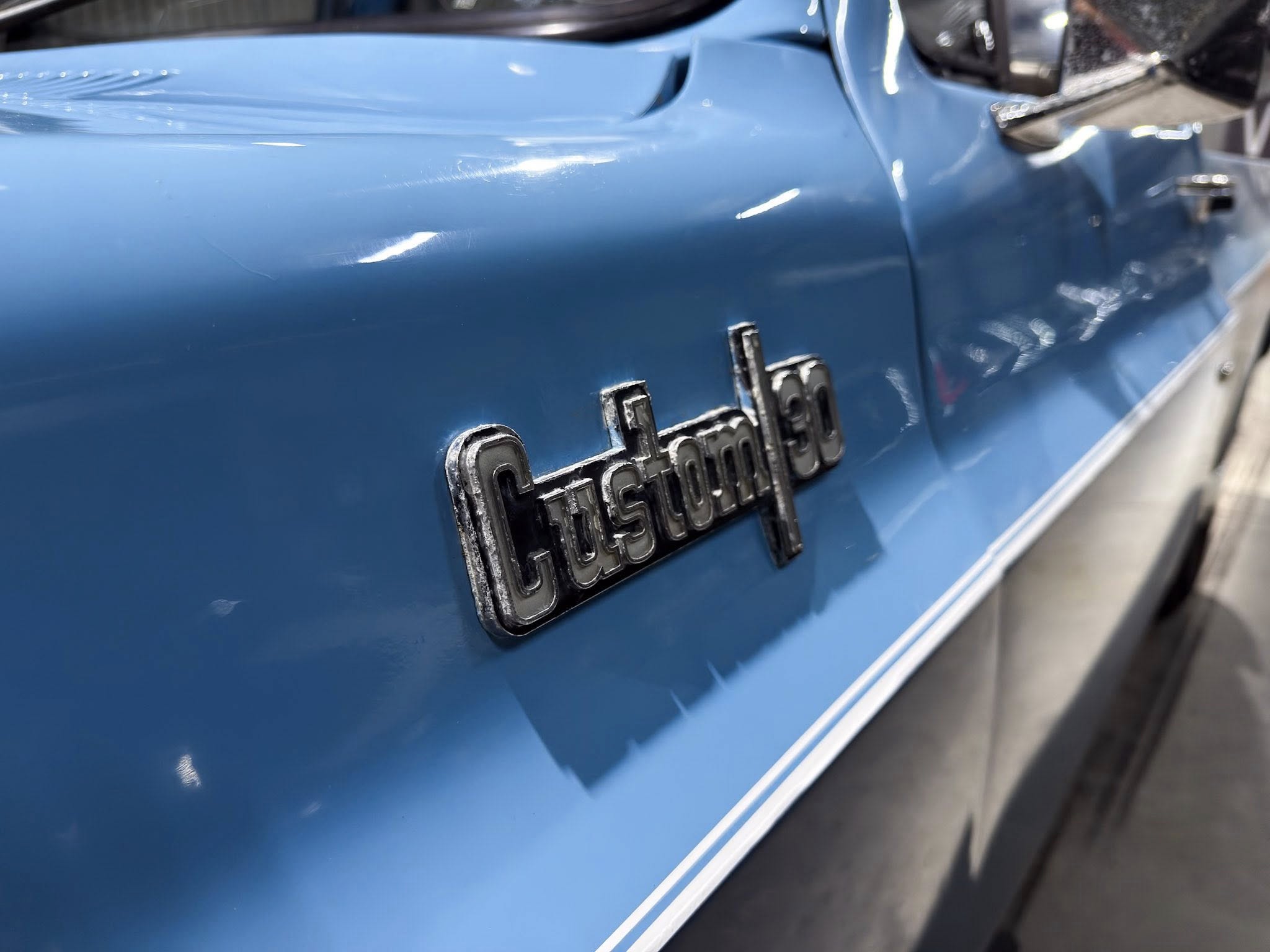 Close-up of a blue car's rear panel with a partially visible chrome badge, reflecting light.