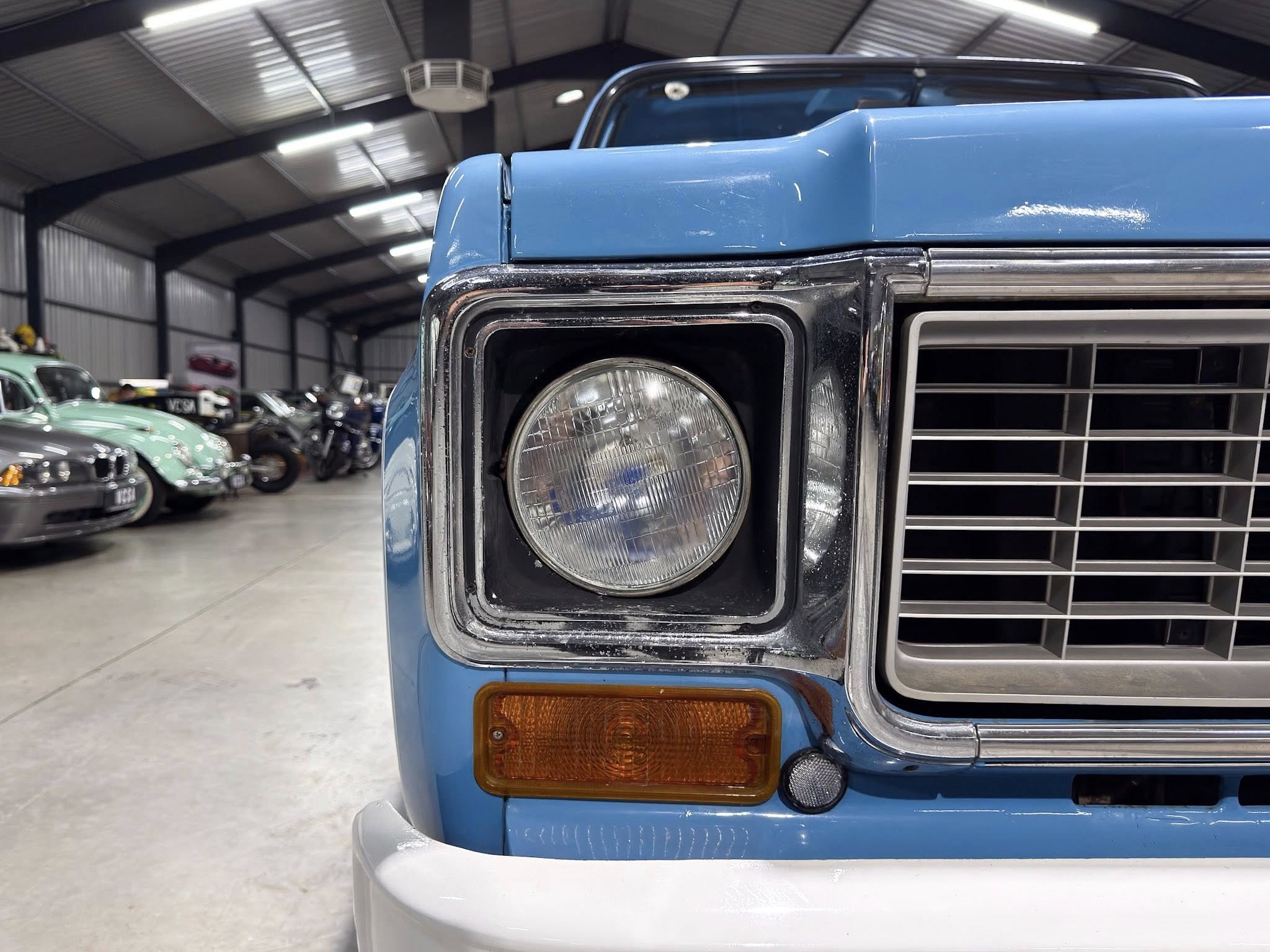 Close-up of the blue front end of a vintage pickup truck with chrome headlight and grille in a showroom-like garage.
