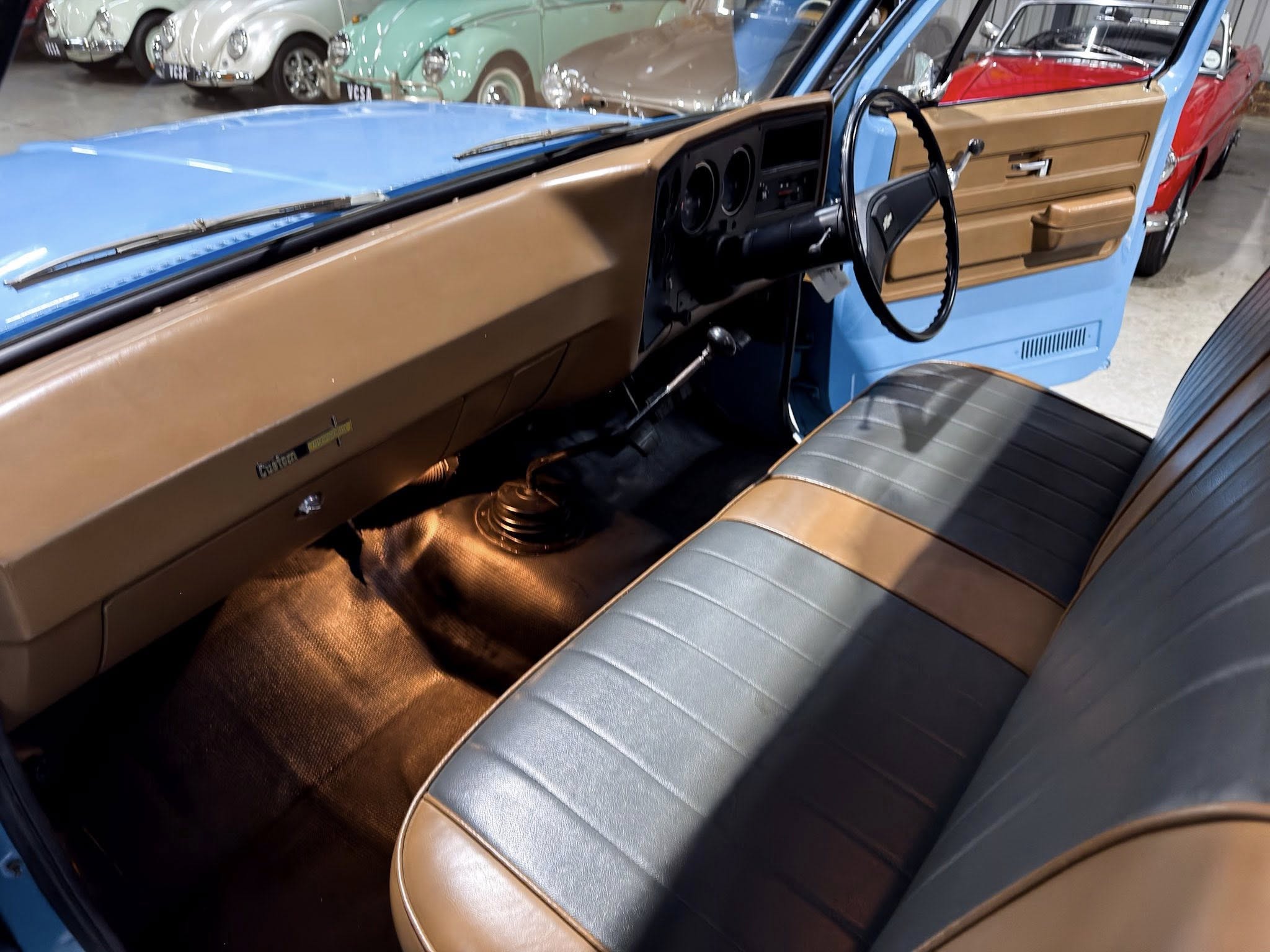 Classic car interior with brown seats and blue exterior, showing the dashboard, steering wheel, and gear shifter in a showroom setting.