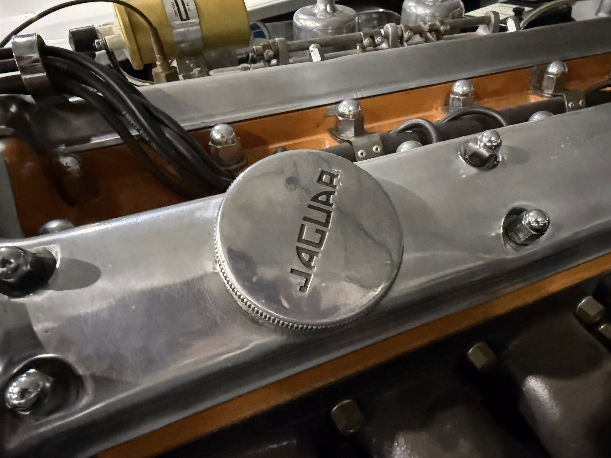 Close-up of a vintage engine bay with polished silver metal components, bolts, and an embossed oil filler cap showing letters.