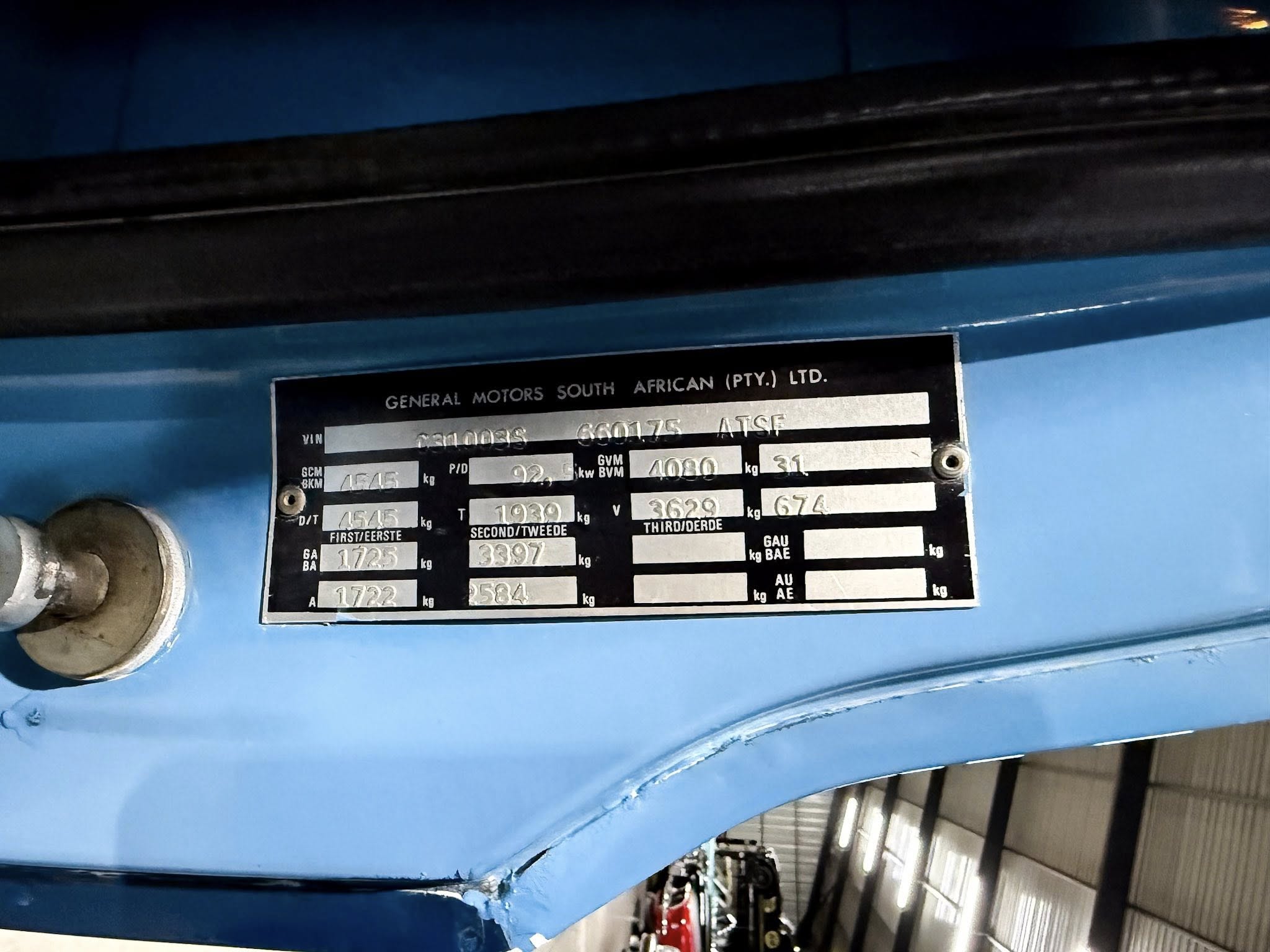 Identification plate on a blue machine displaying General Motors South Africa (Pty.) Ltd. and vehicle specs (VIN and weights).