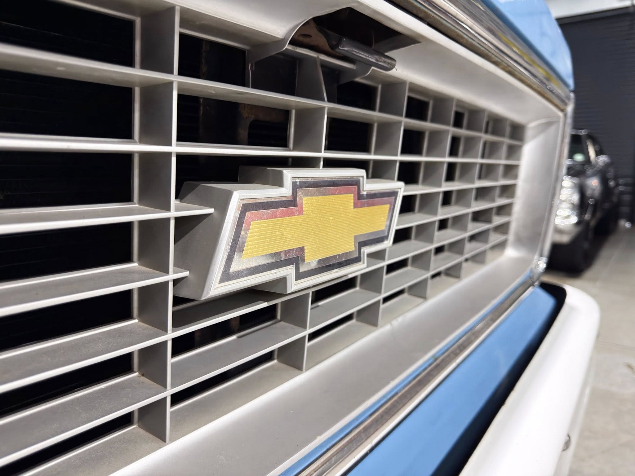 Close-up of a Chevrolet front grille with the gold bowtie emblem on a blue vehicle.