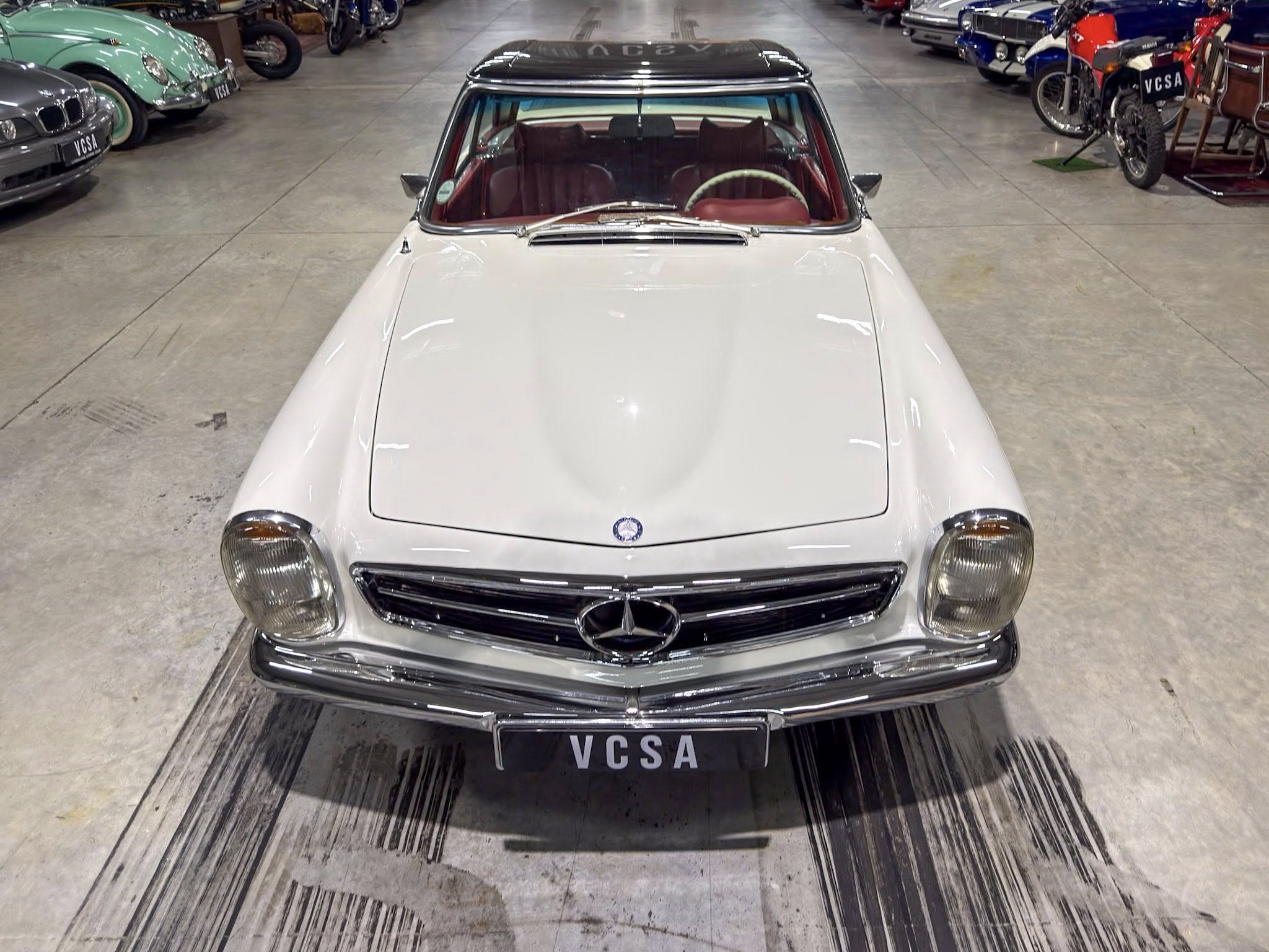 Front view of a white vintage Mercedes in a showroom with other classic cars along the sides.