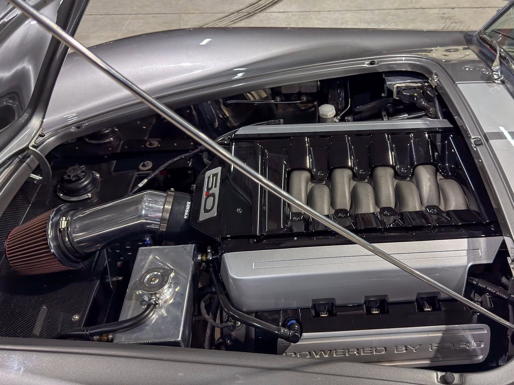 Engine bay view with a large aftermarket air intake and a 'Powered by Ford' badge on the firewall.