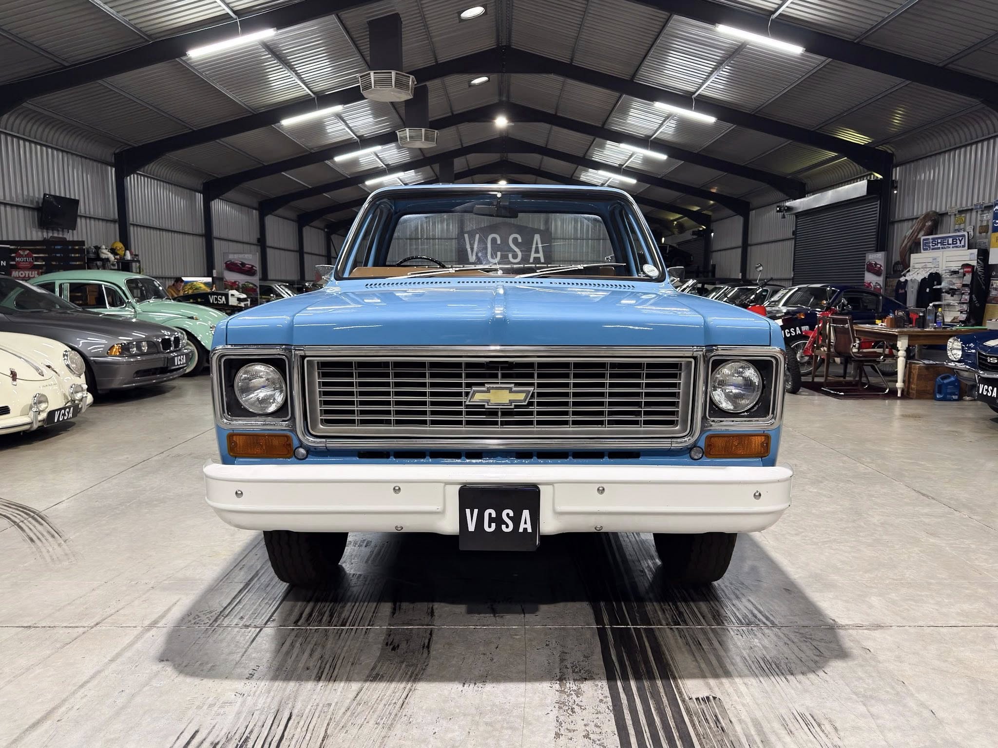 Front view of a blue vintage Chevrolet pickup inside a showroom, surrounded by other classic cars.