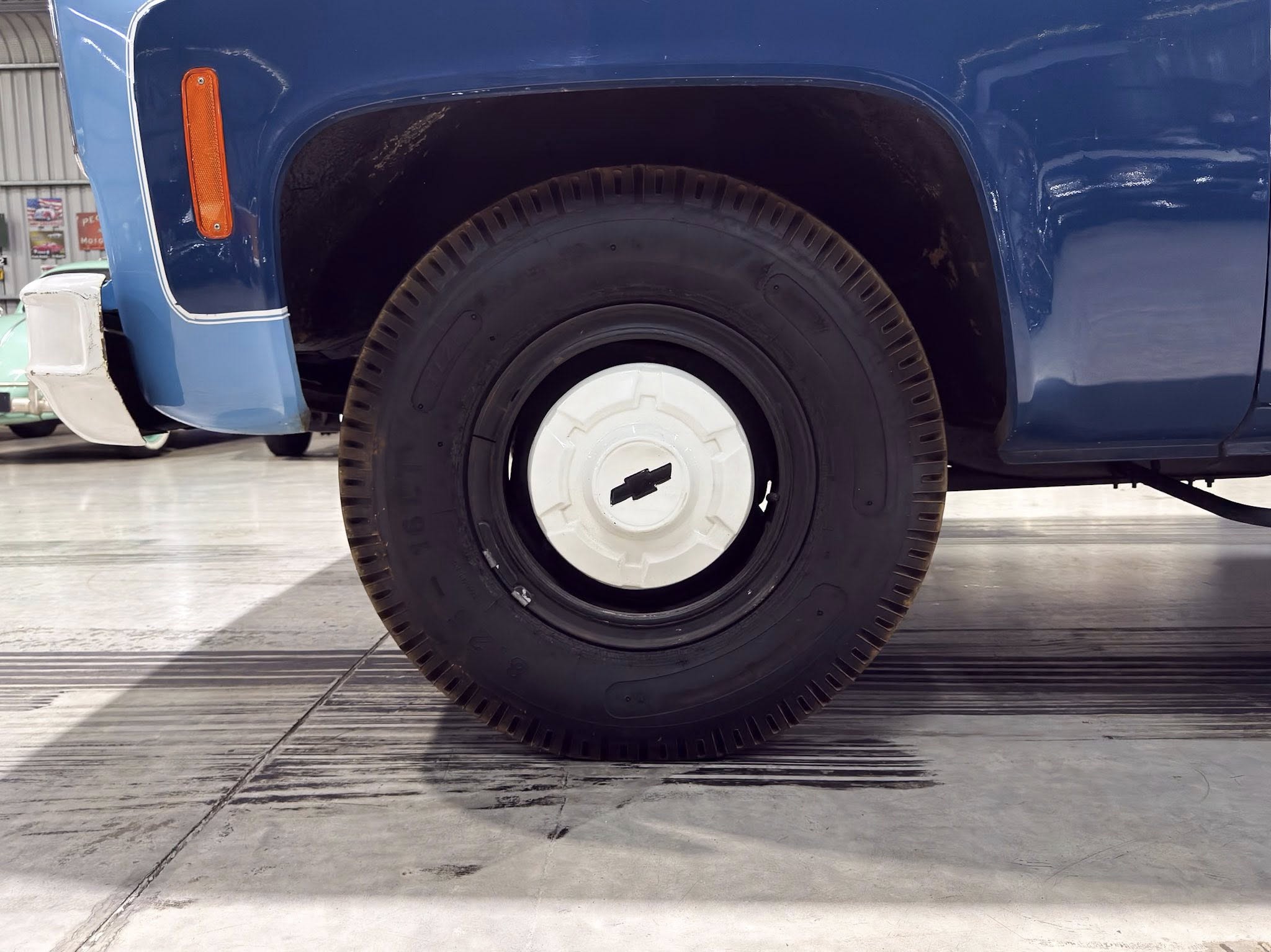 Blue truck wheel area: tire in a blue fender with an orange side marker light and white hubcap in a showroom setting.
