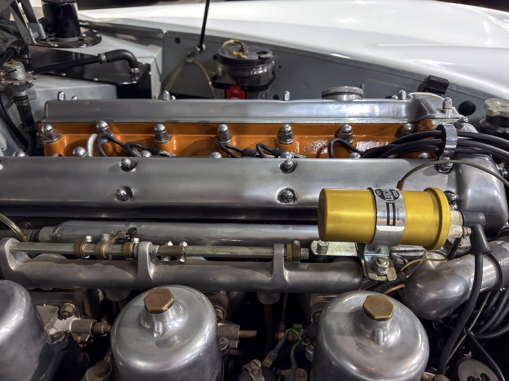 Engine bay with orange valve cover, silver intake manifold, and yellow ignition coil among hoses and bolts.