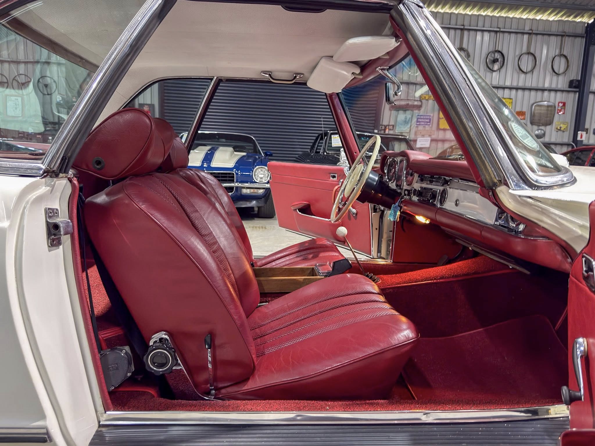 Red leather car interior with an open driver-side door, tan headliner, and steering wheel visible in a classic car showroom.