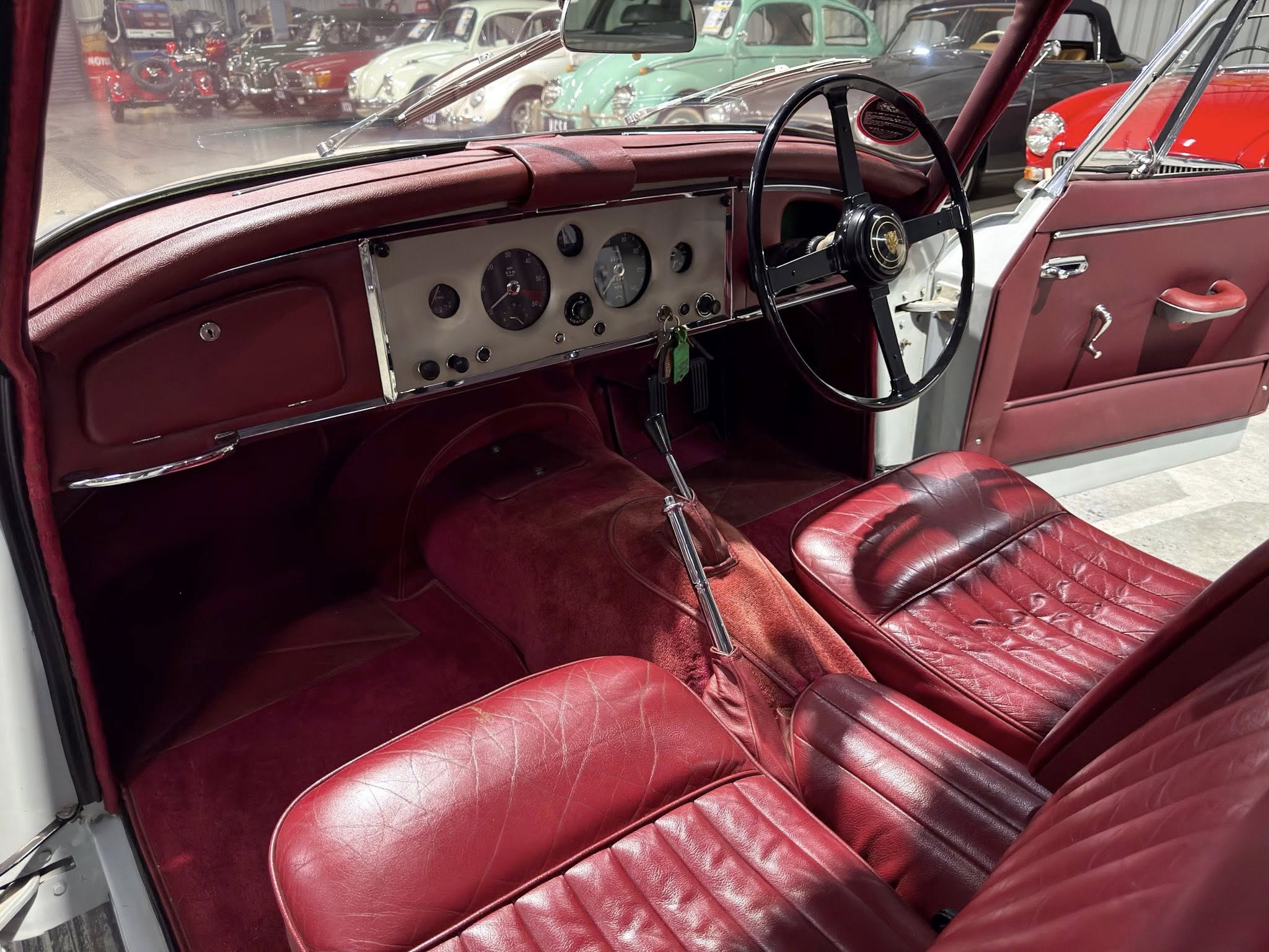 Interior of a vintage red-leather car showing a classic gray dashboard and large black steering wheel