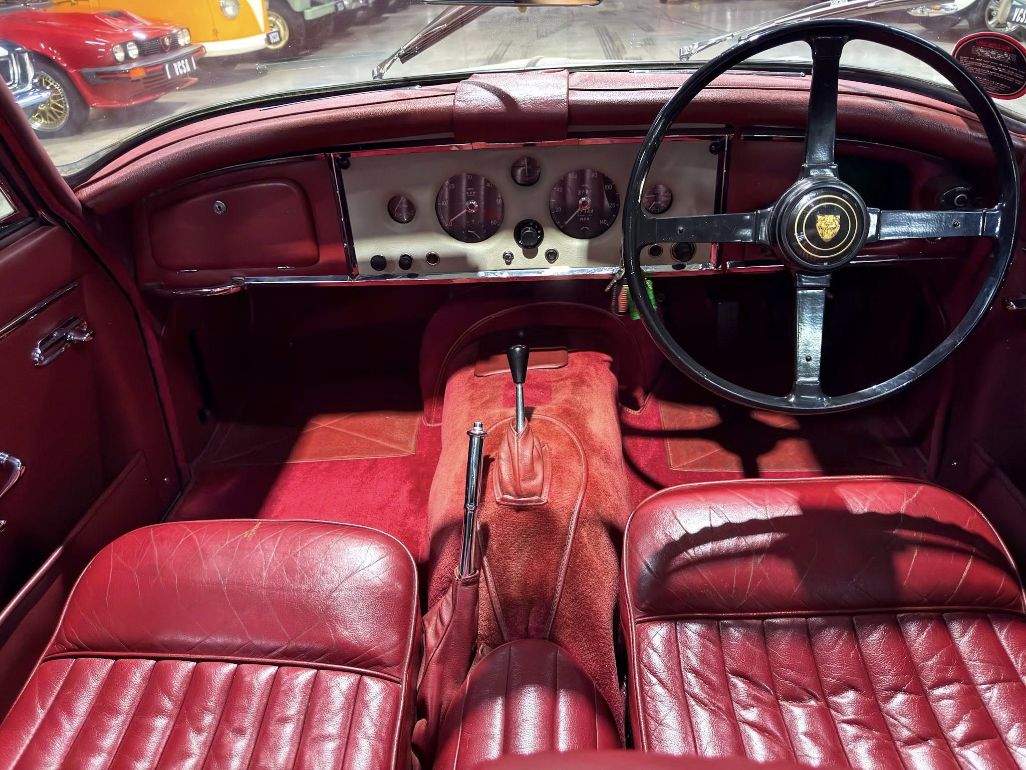 Classic car interior with red leather seats, red dashboard, and a large black steering wheel.
