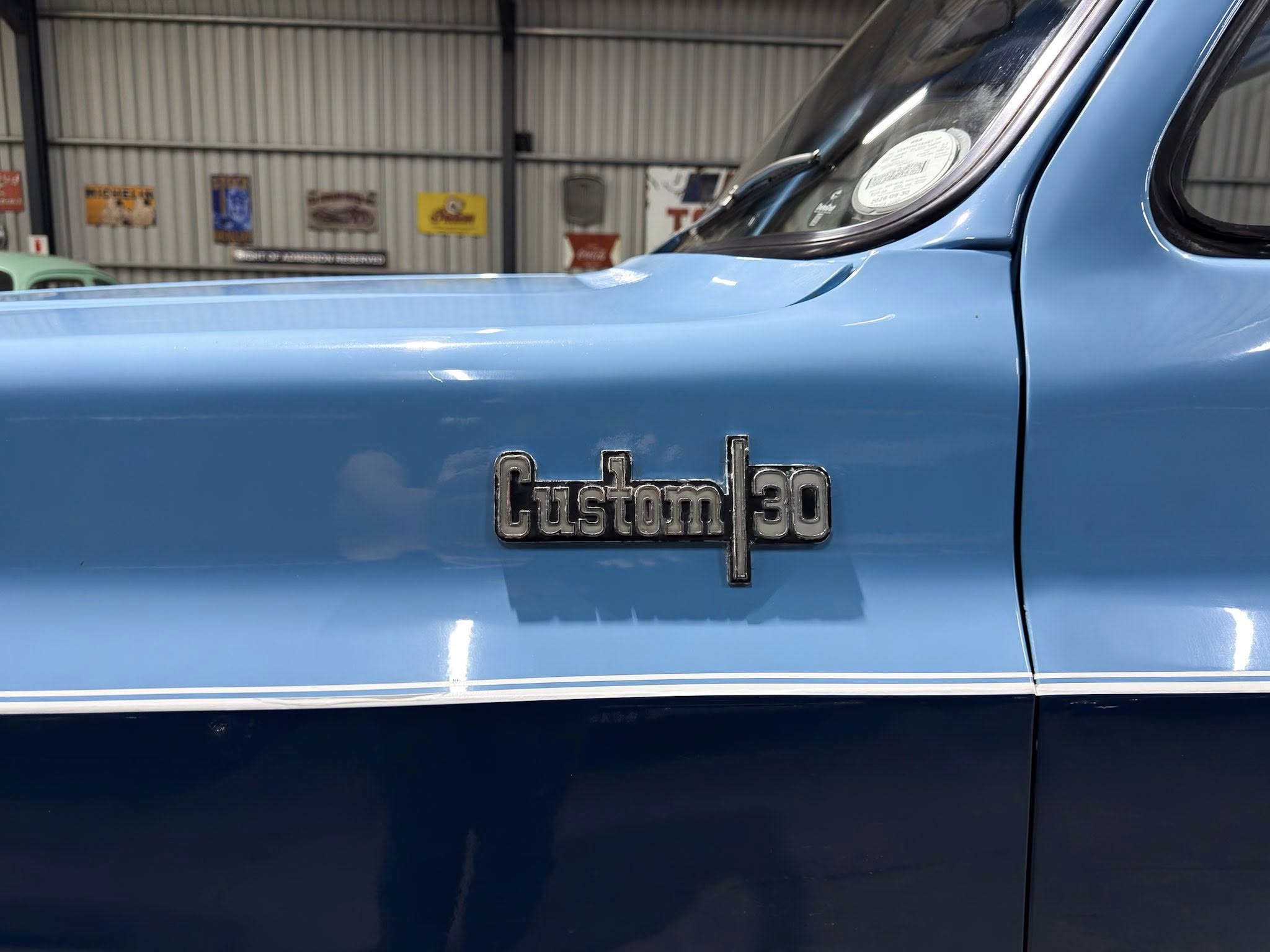 Side view of a light blue vintage pickup truck featuring a chrome 'Custom 30' badge on the door. In a workshop background.