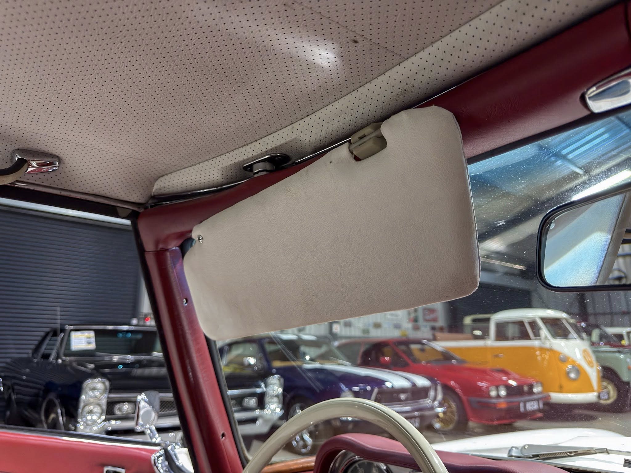 Beige perforated headliner and sun visor inside a red car, with other showroom vehicles visible through the windshield.