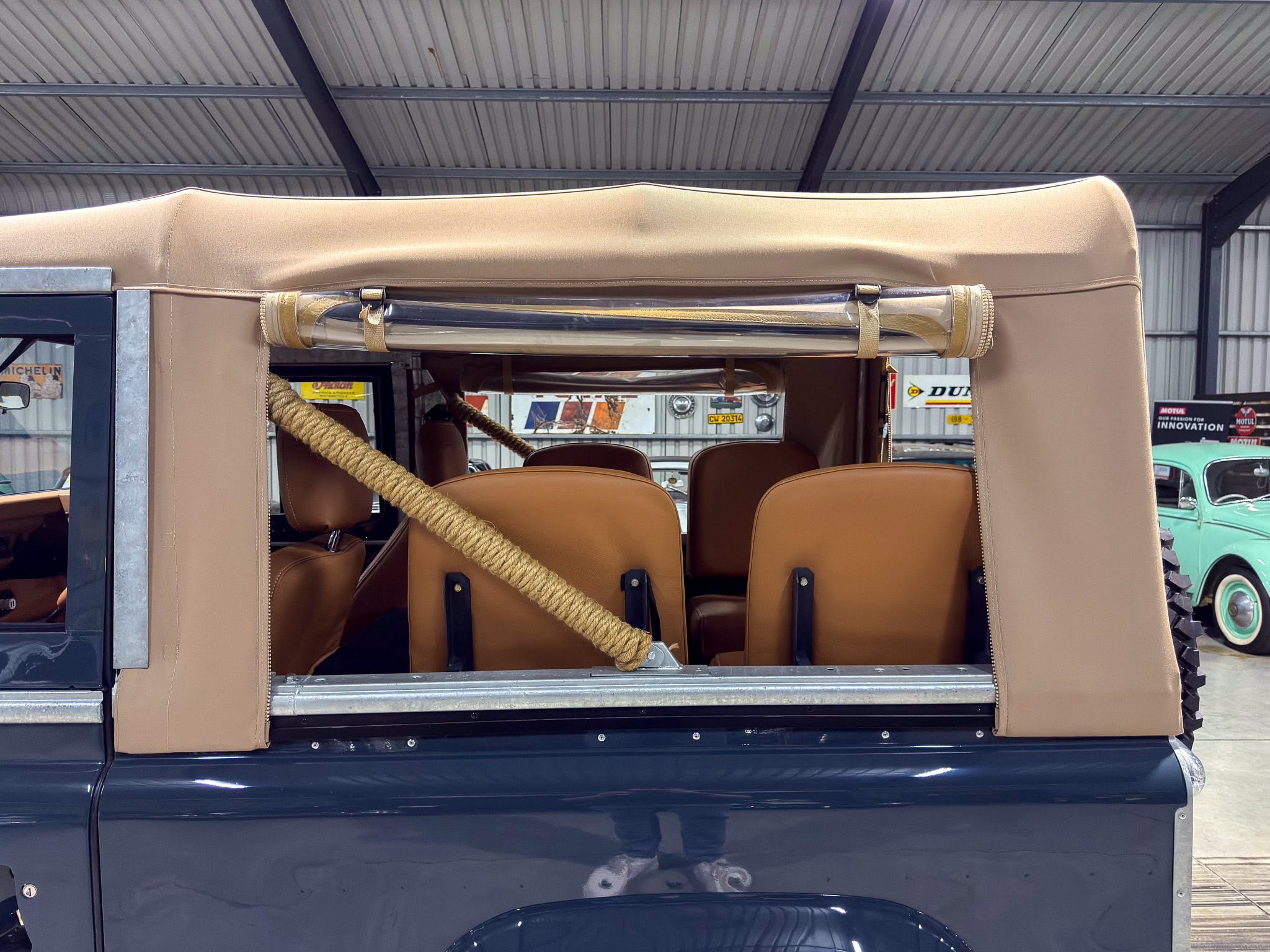 Open-top vintage vehicle with a tan canvas roof, brown leather seats, and coiled rope inside.