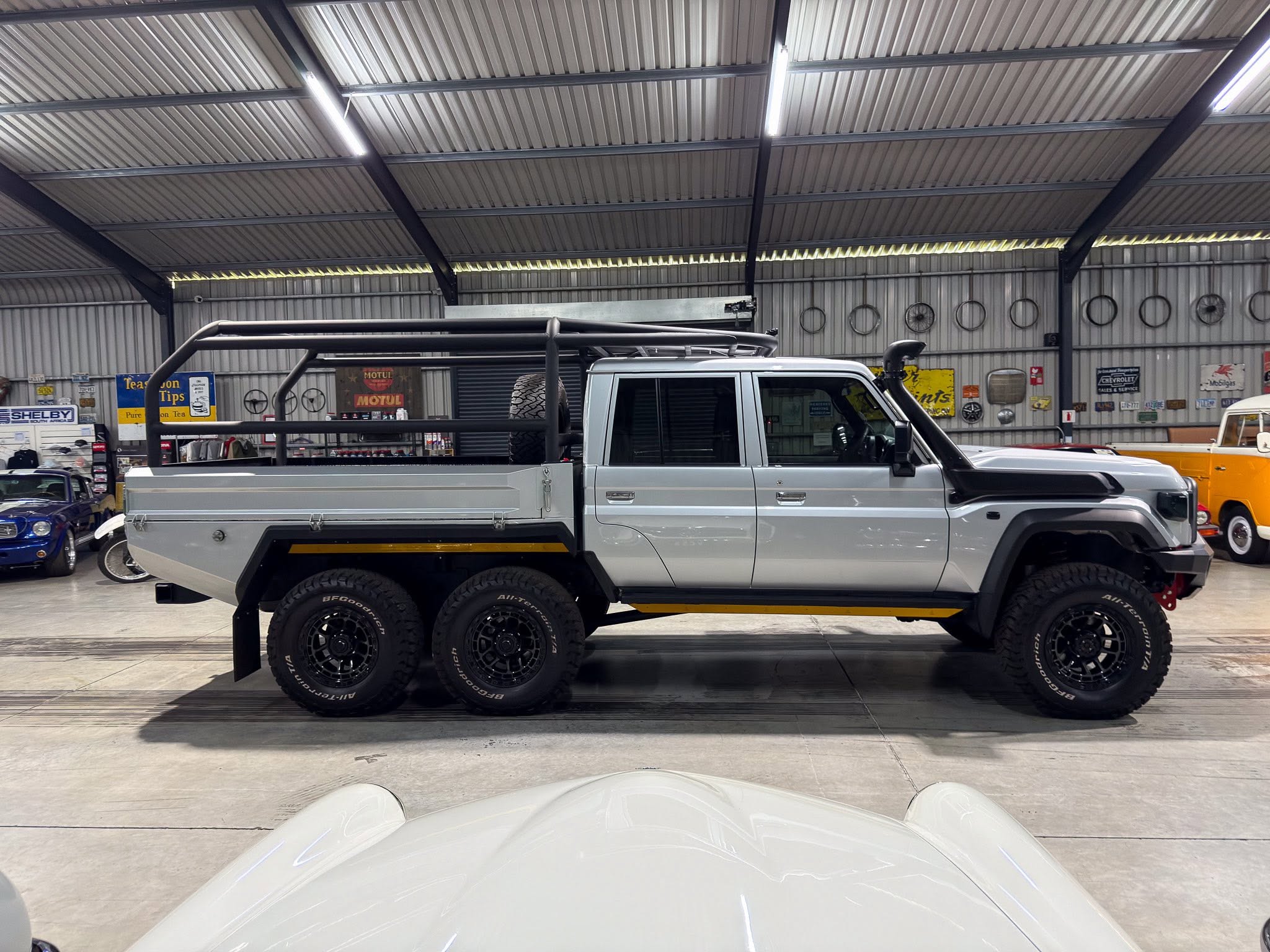 Interior of a workshop with a gray pickup on a flatbed and other vehicles in the background. Industrial metal ceiling and signs on the wall.