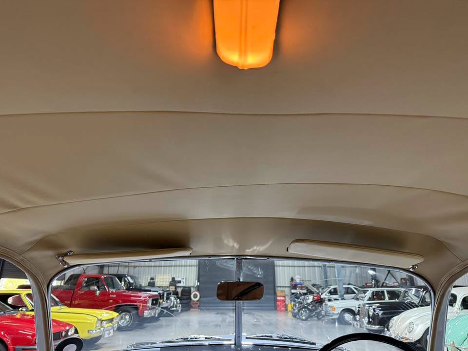 Interior of a vintage car, view through the windshield to a showroom full of classic cars, with an orange dome light overhead