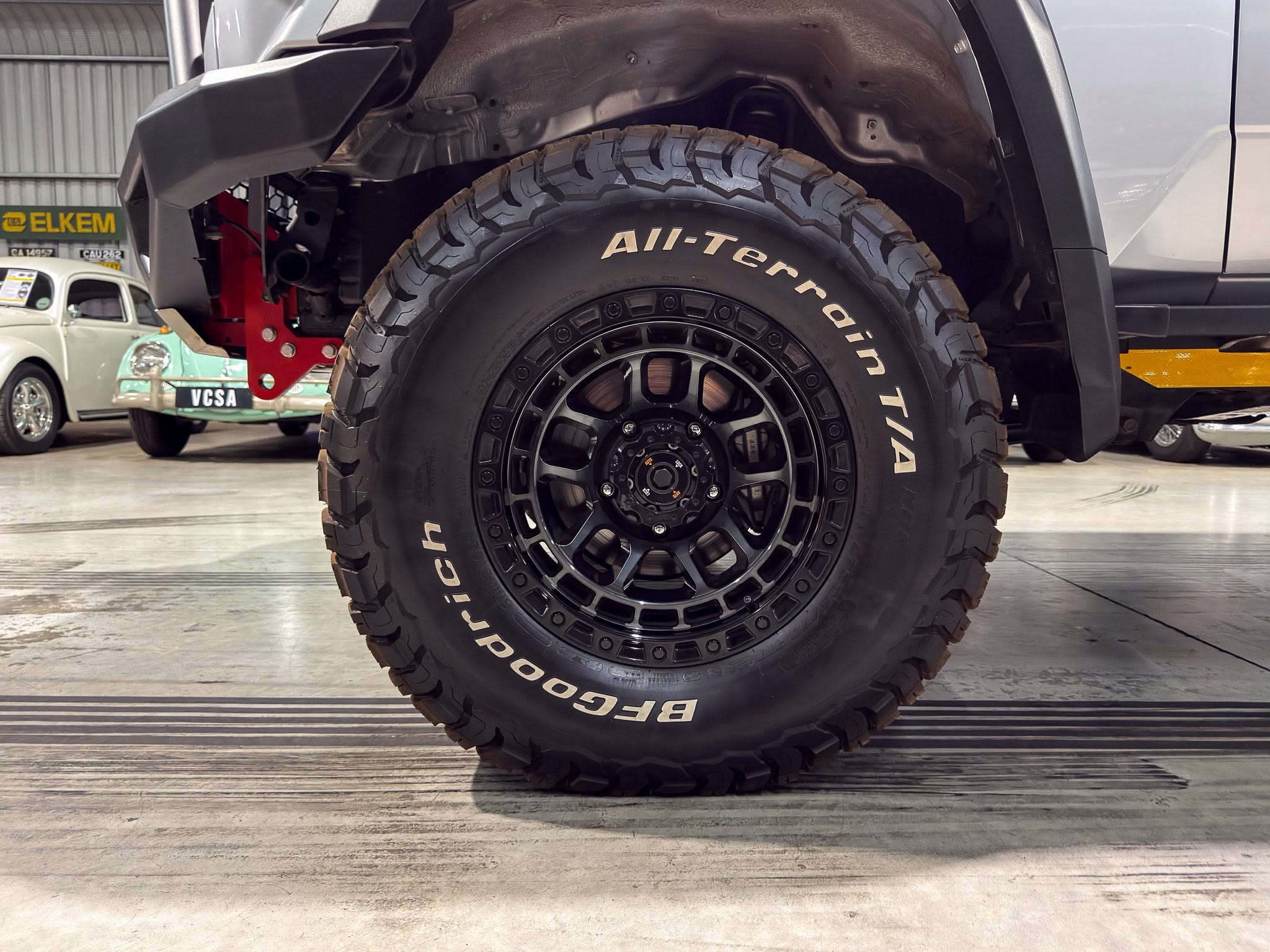 Close-up of a large all-terrain tire and black rim on a raised off-road vehicle in a workshop.