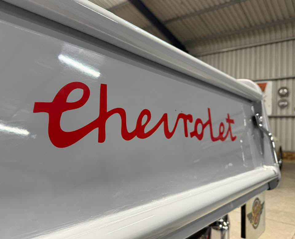 Close-up of a white vehicle side panel with red Chevrolet script logo in a workshop setting.