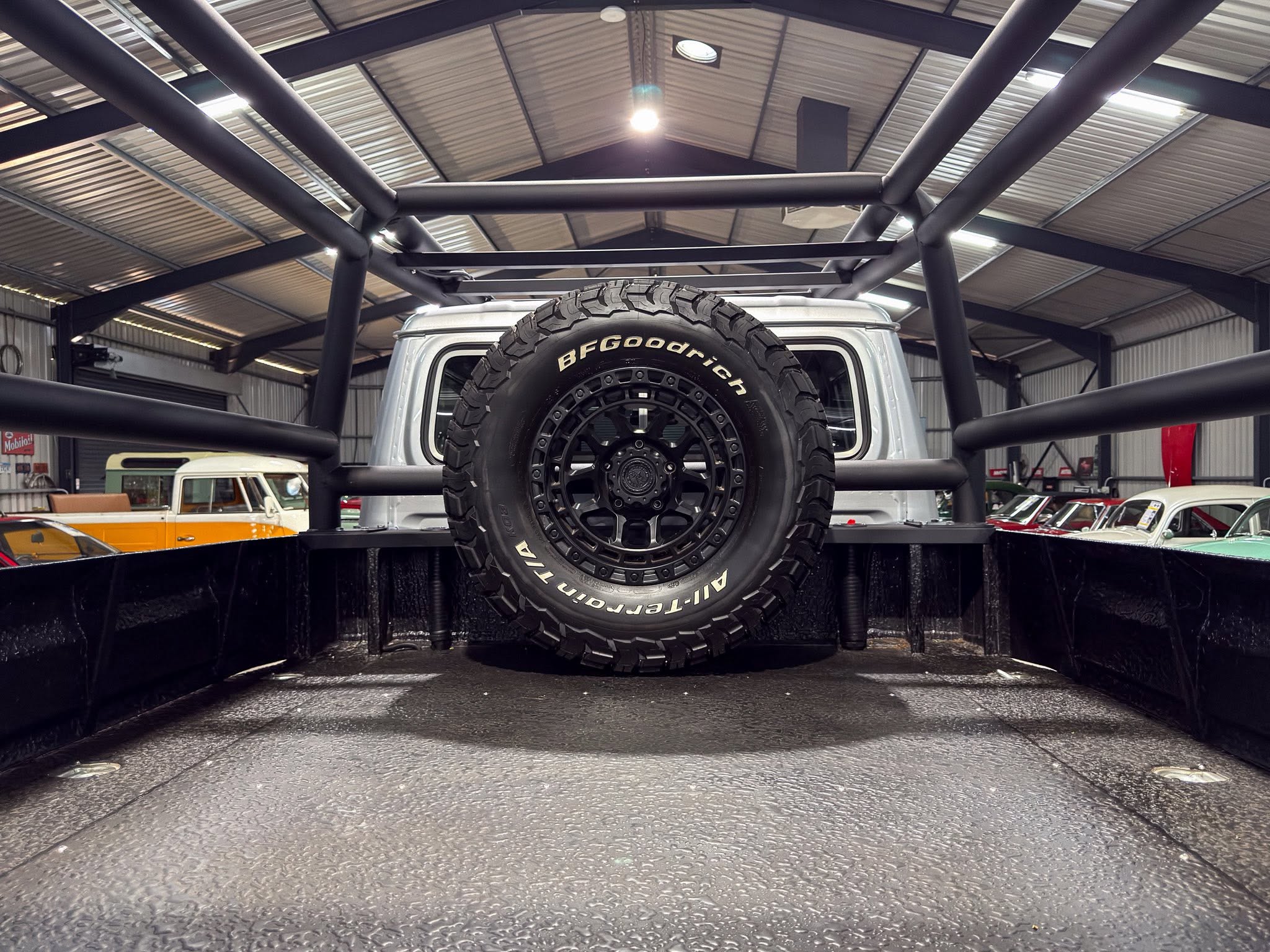 Vehicle with a large off-road tire mounted at the rear inside a metal-framed garage or workshop