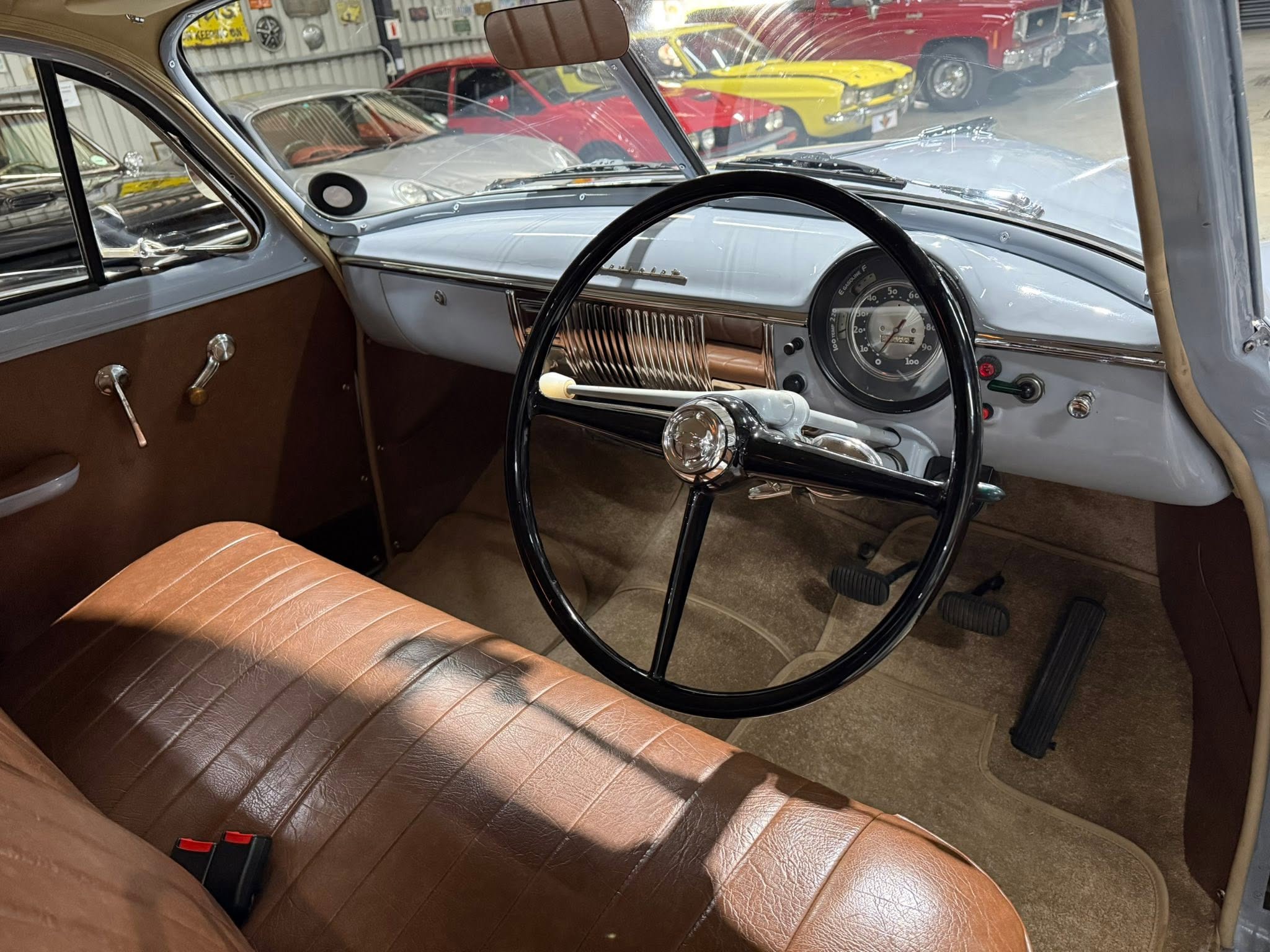 Interior of a vintage car with brown leather seats, chrome dashboard, and large black steering wheel.
