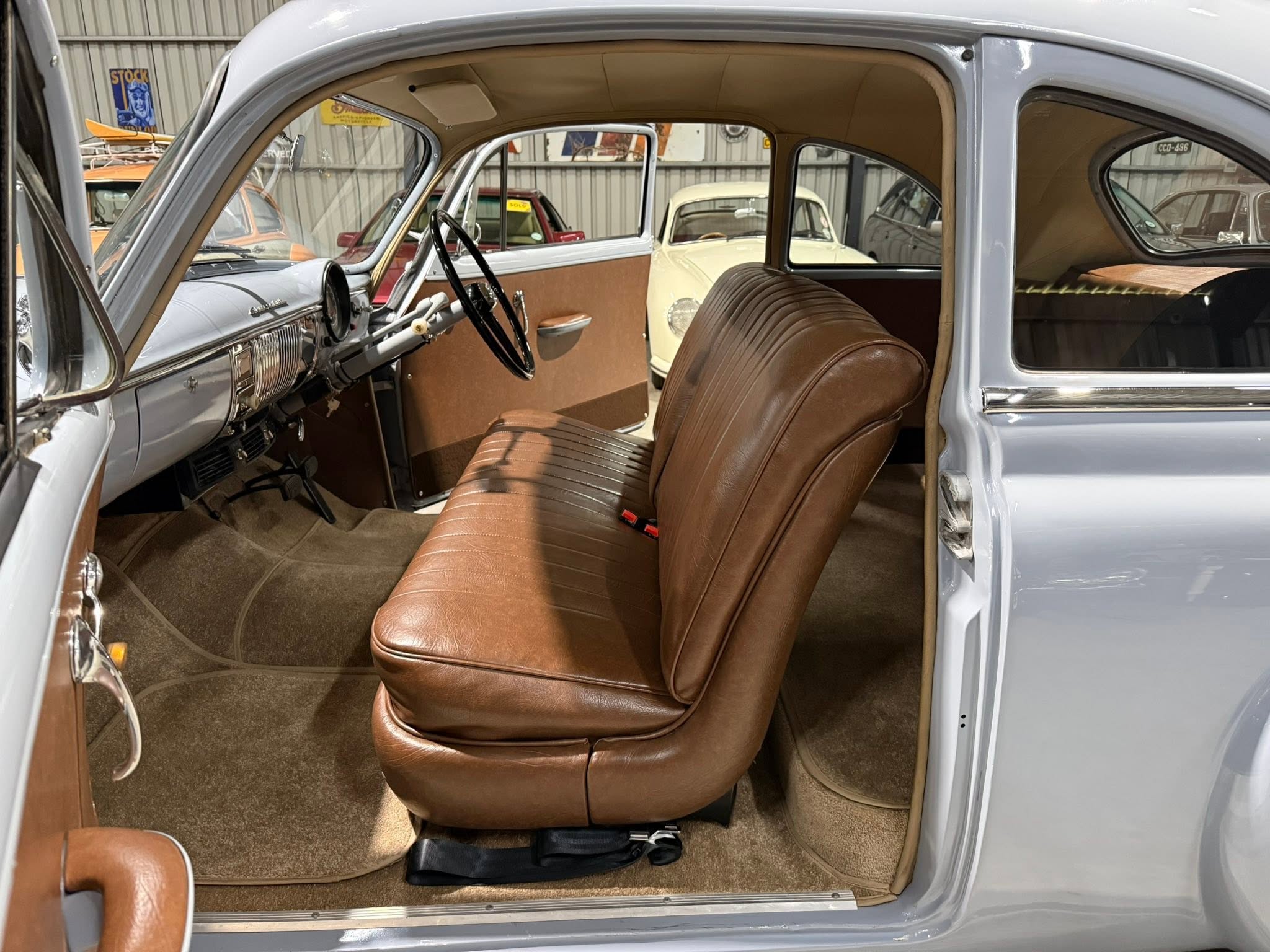 Interior of a vintage car with brown leather seats, light blue exterior, and a visible steering wheel and dashboard