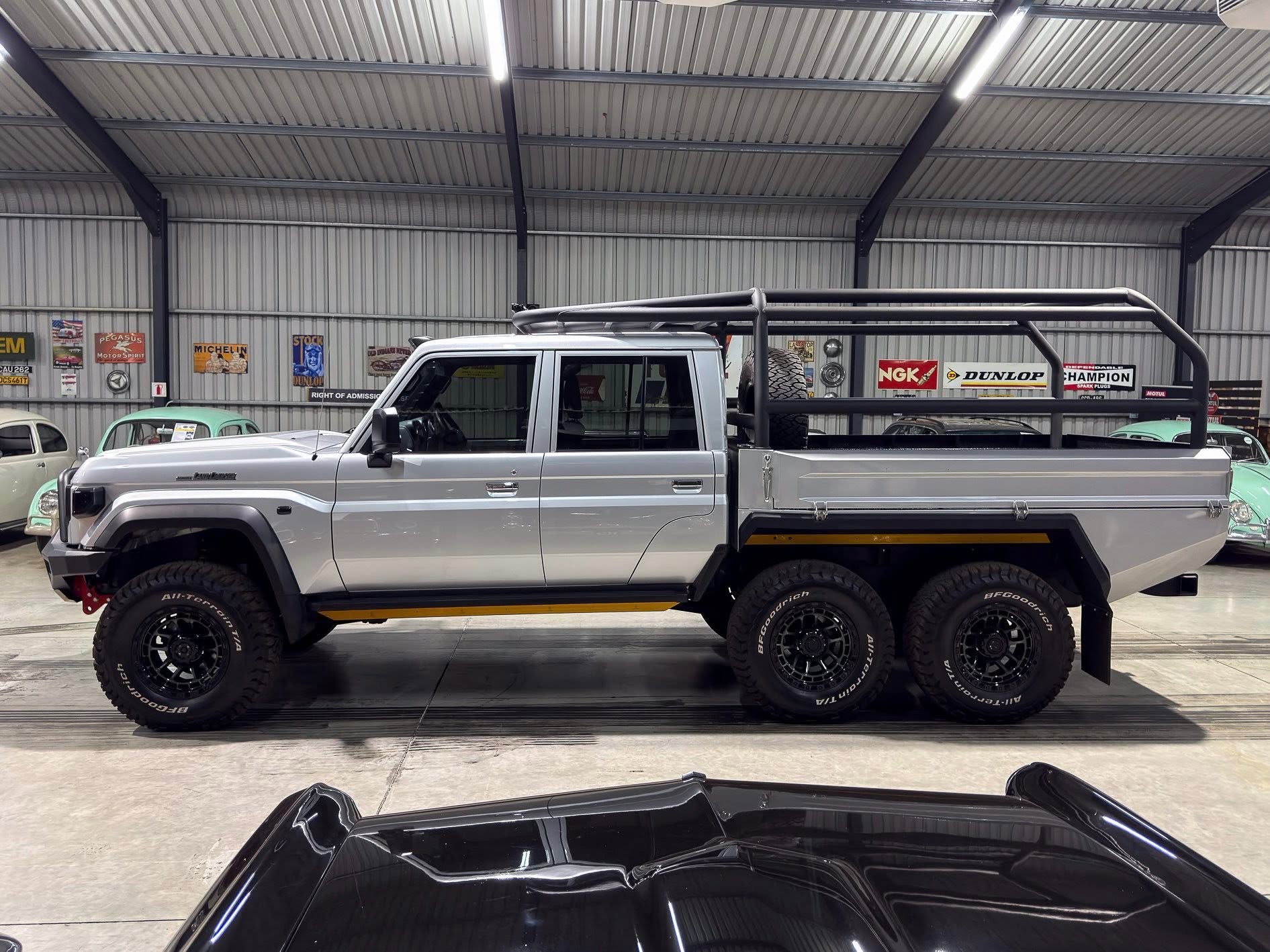 Silver pickup with a metal roll cage on the bed, parked inside a showroom with vintage signs on the walls.